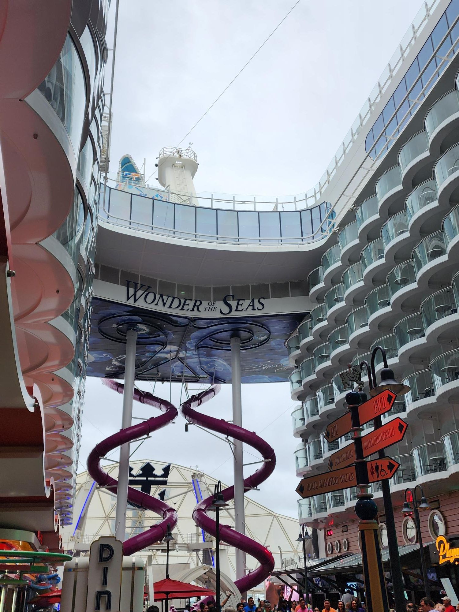 View of a cruise ship docked at a port with a large sign reading 'World's Best.' The image includes a pink slide and colorful structures.