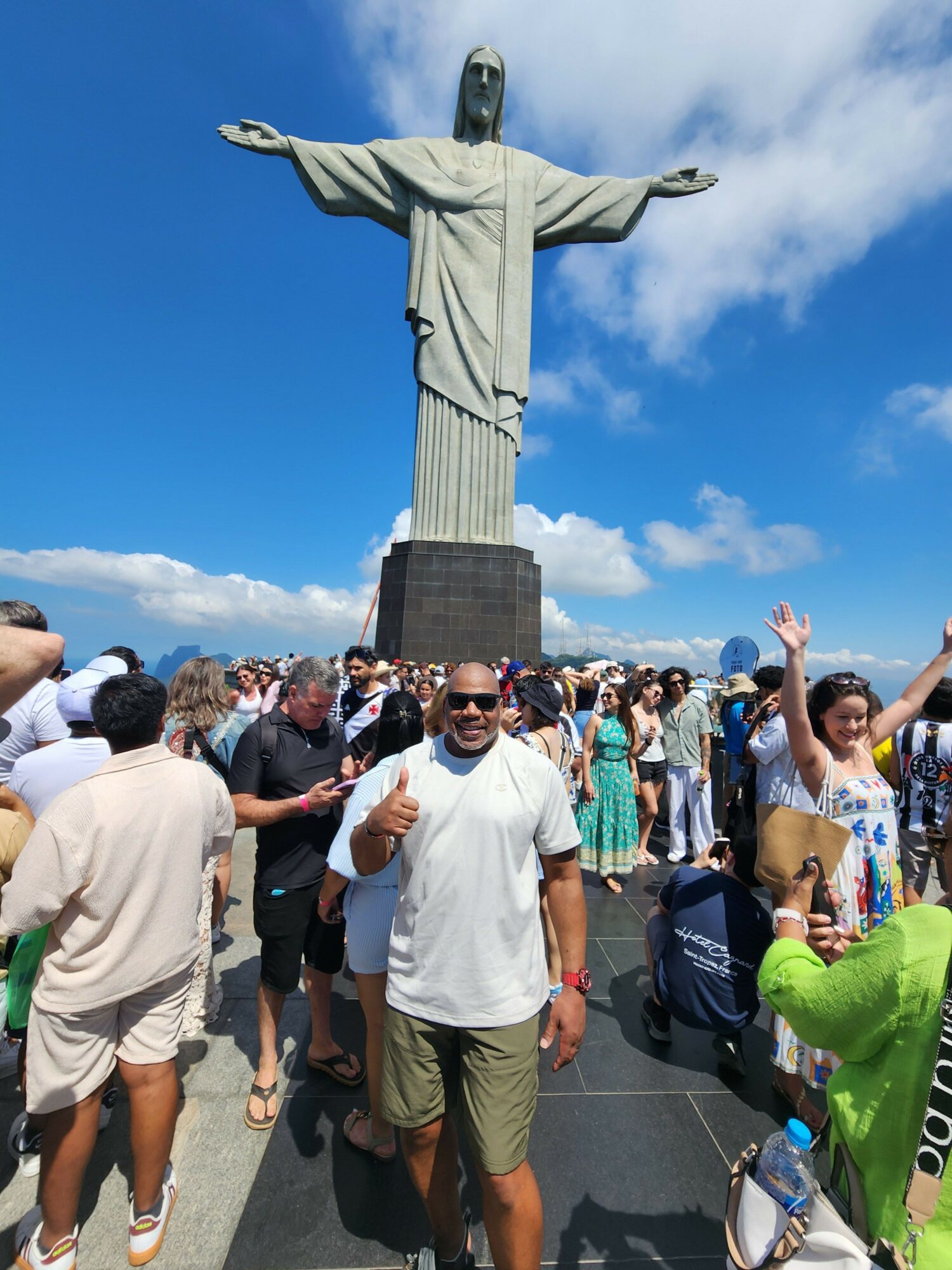 People gather around a replica of the Statue of Liberty's torch on a sunny day with blue sky and clouds.