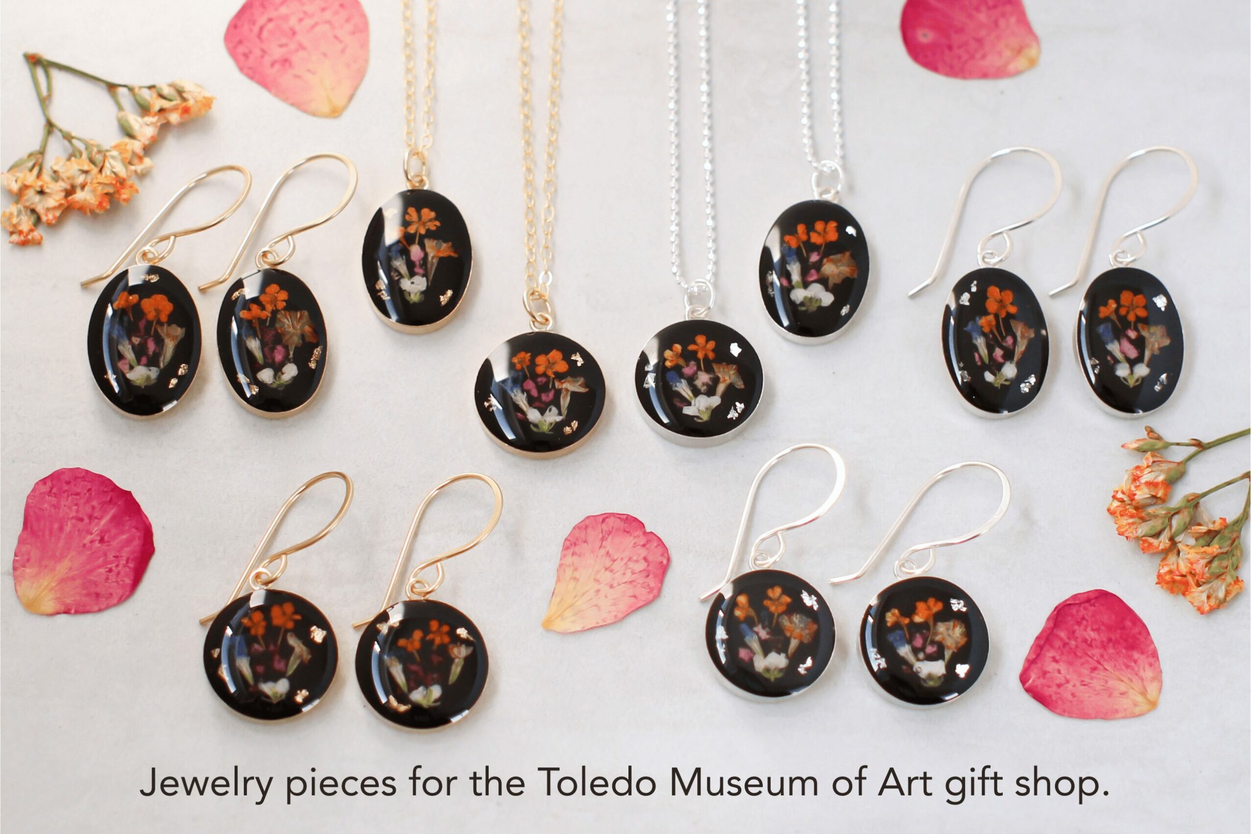 Set of black jewelry pieces with floral designs, including earrings and necklaces, arranged on a white surface with scattered flower petals.