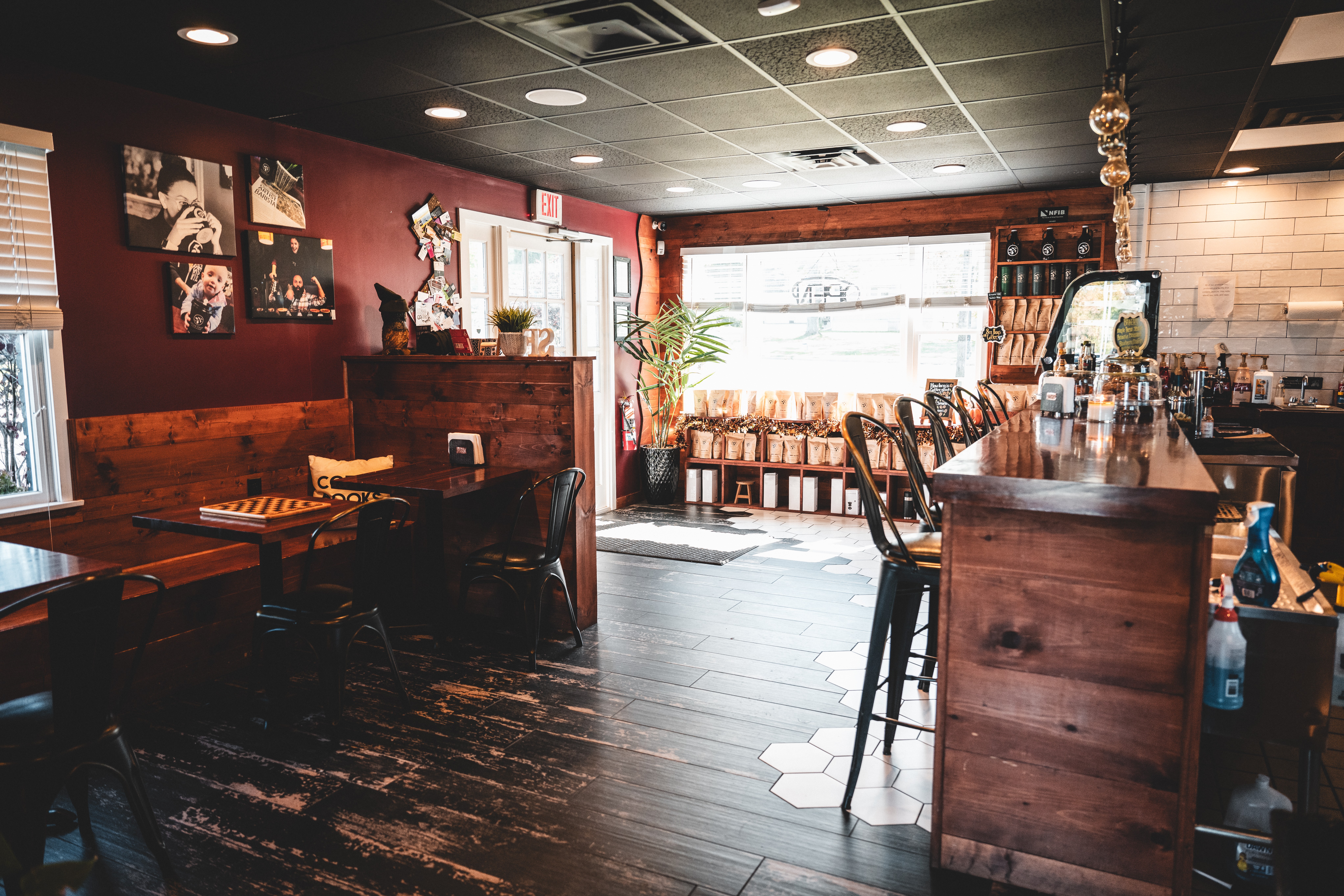 Interior of a cozy cafe with wooden furniture, a bar counter, and decorative wall art, illuminated by natural light from windows.