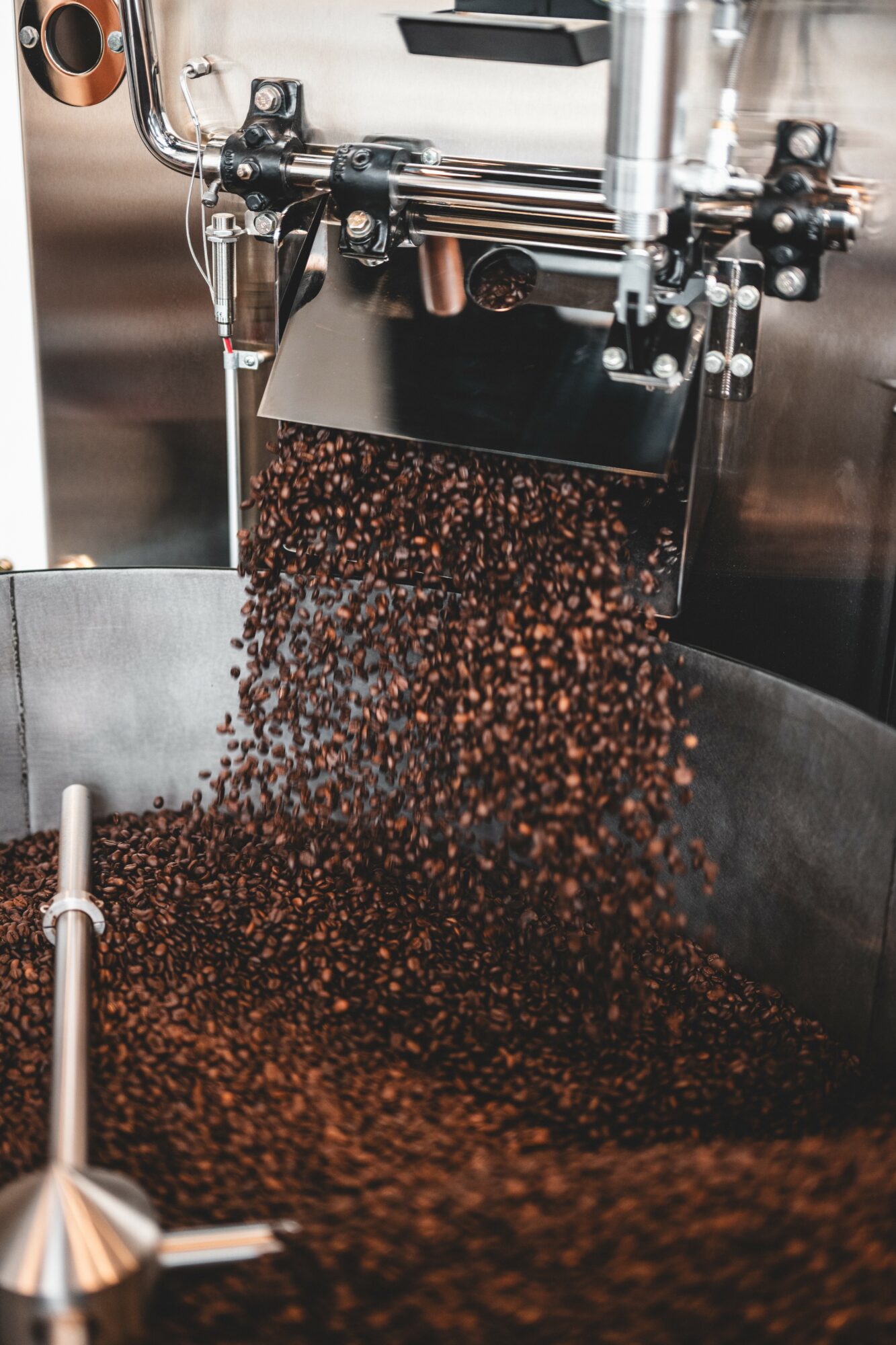 Coffee beans falling from a machine into a container, with metallic parts visible in the background.