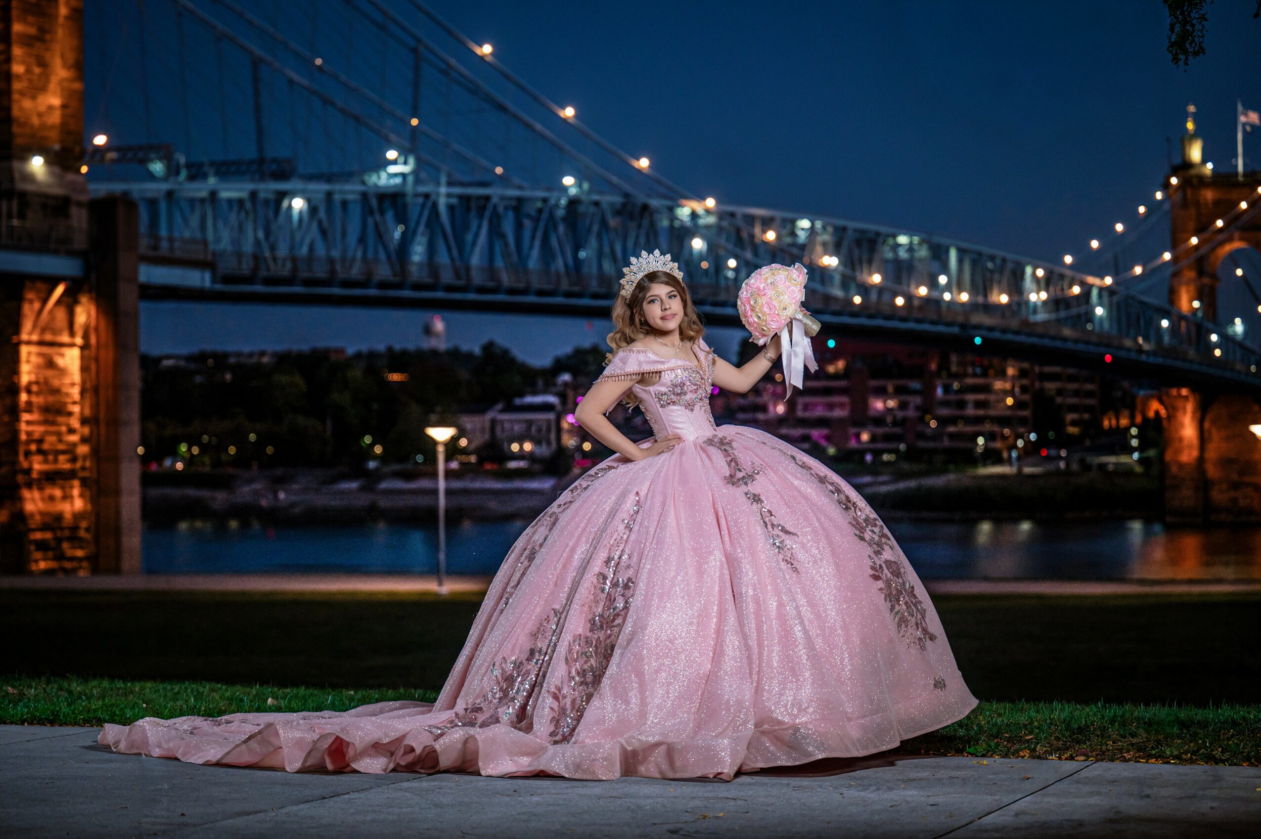 Young woman in pink ball gown holding a pink cotton candy under a bridge at night.