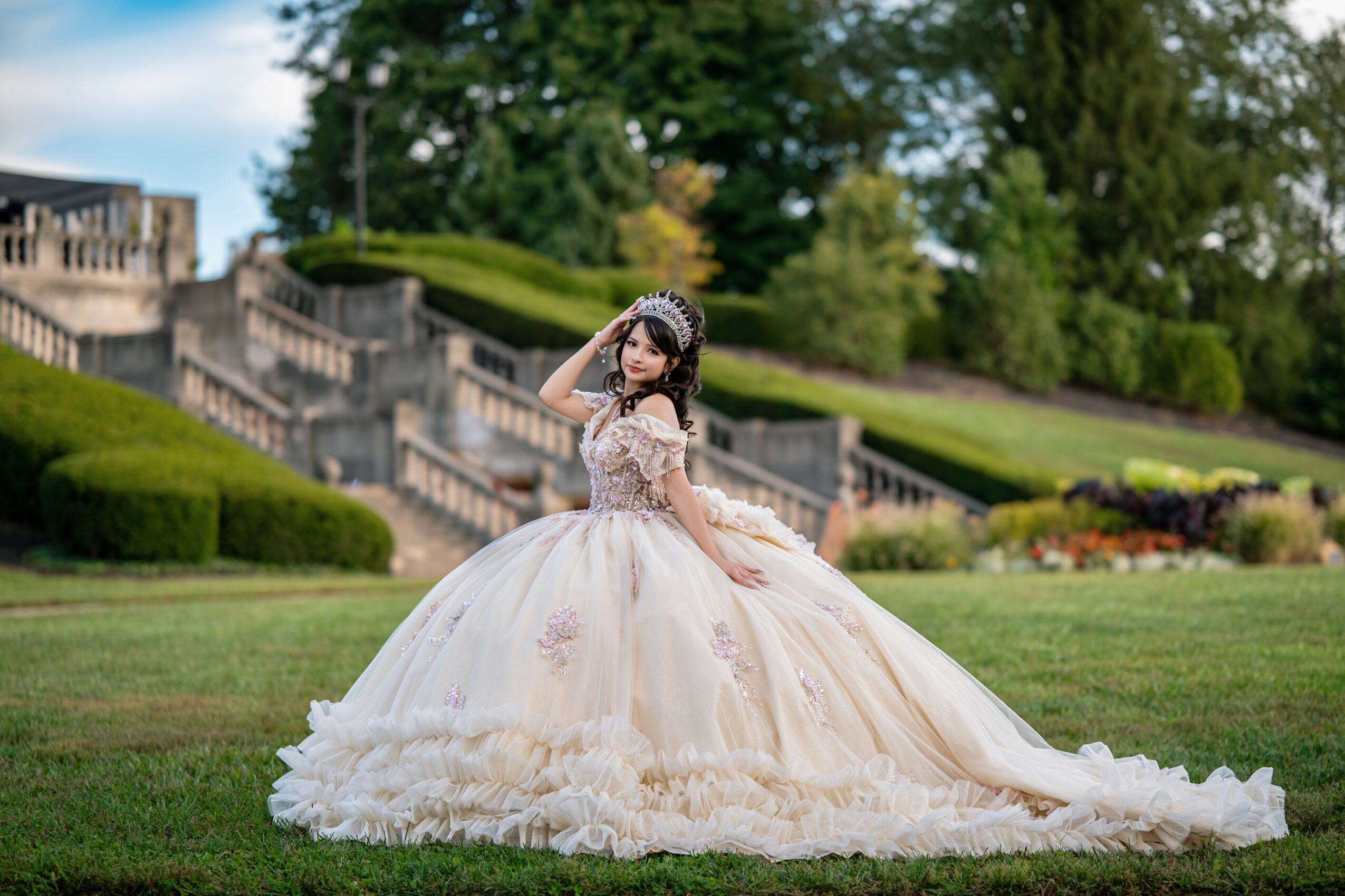 Woman in a wedding dress standing on grass with a garden and stairs in the background.