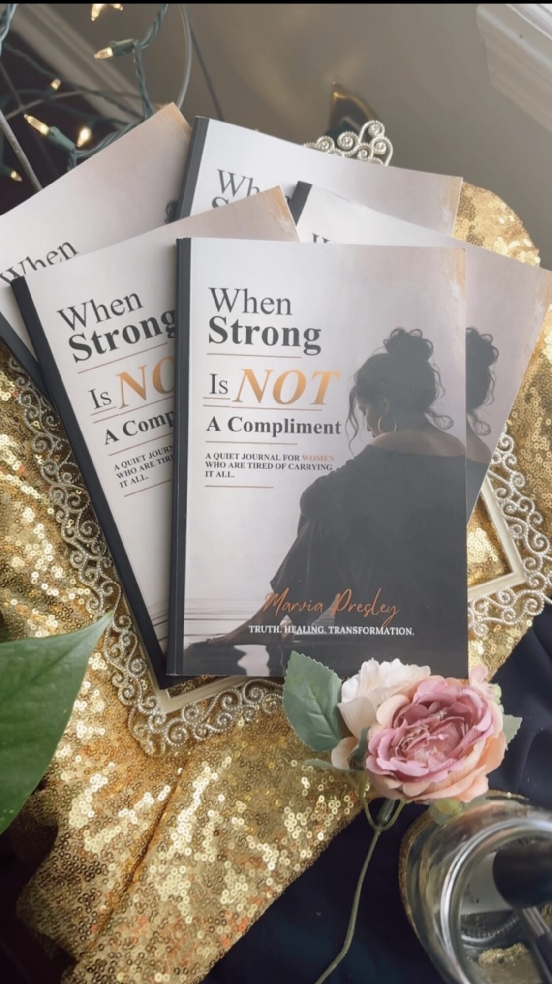 Three copies of a book titled 'When Strong Is NOT A Compliment' with a woman on the cover, surrounded by flowers and decorative items.