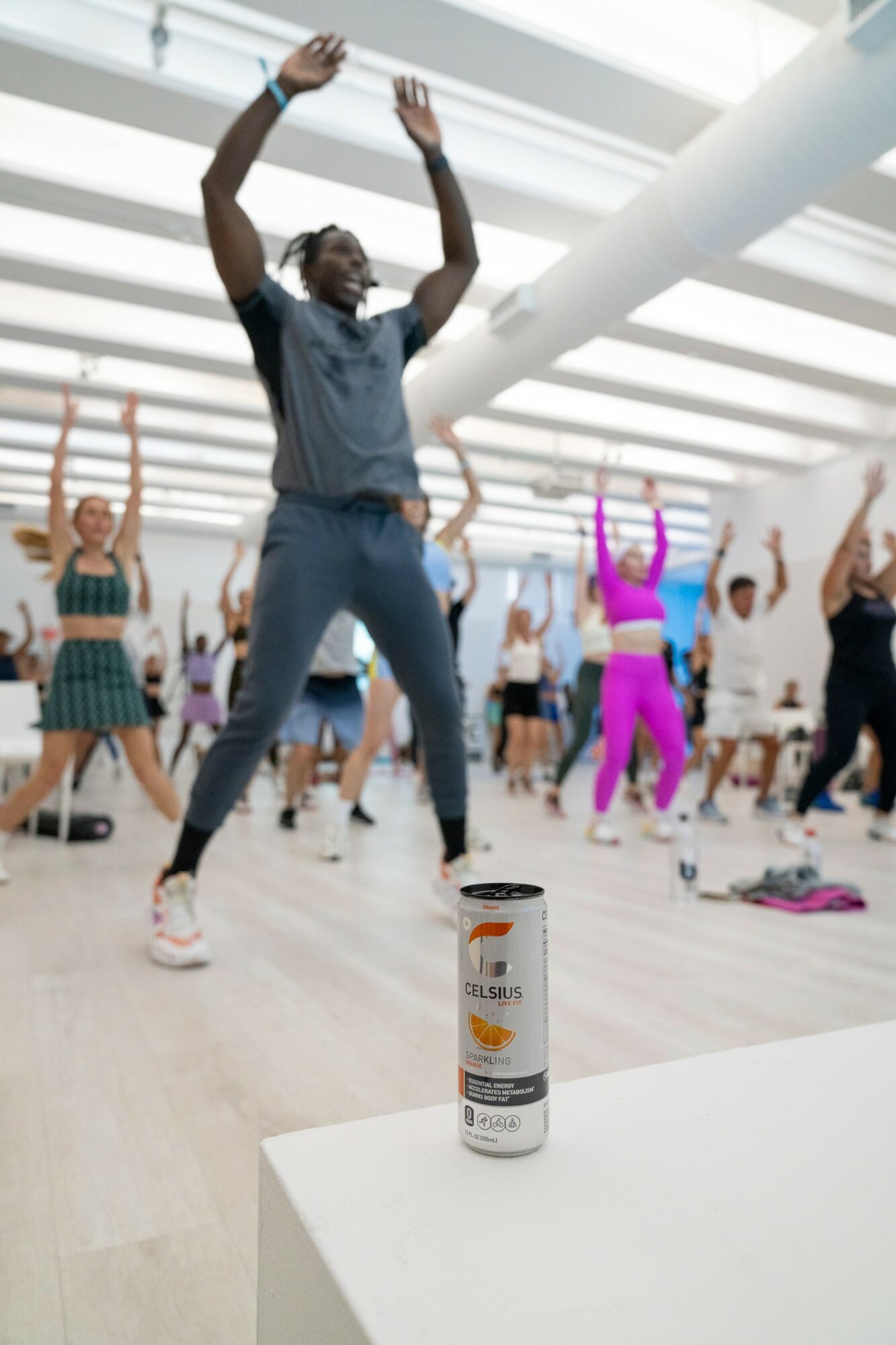 Group of people participating in a dance class in a bright studio, with a can on a white table in foreground.