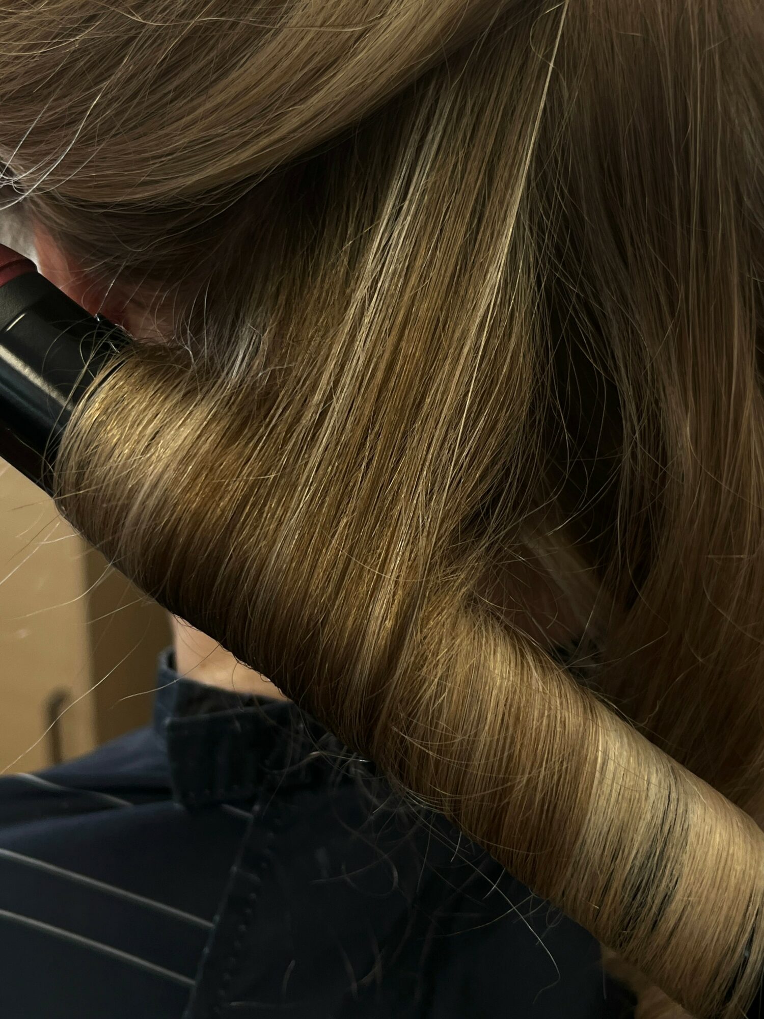 Close-up of a person with straight, light brown hair being styled with a curling iron.