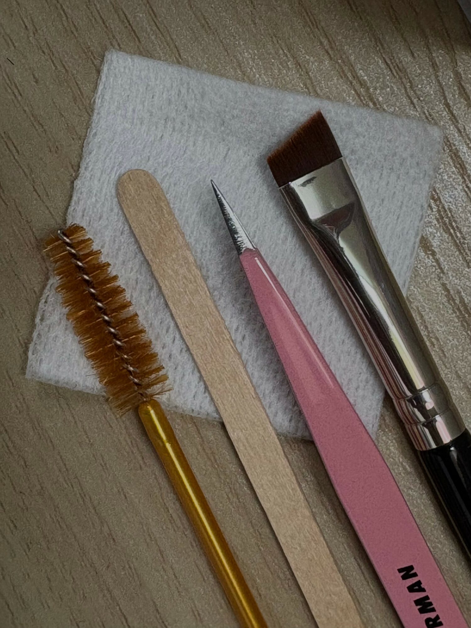 Tools including a small brush, wooden spatula, metal spatula, and a pink spatula on a white cloth.