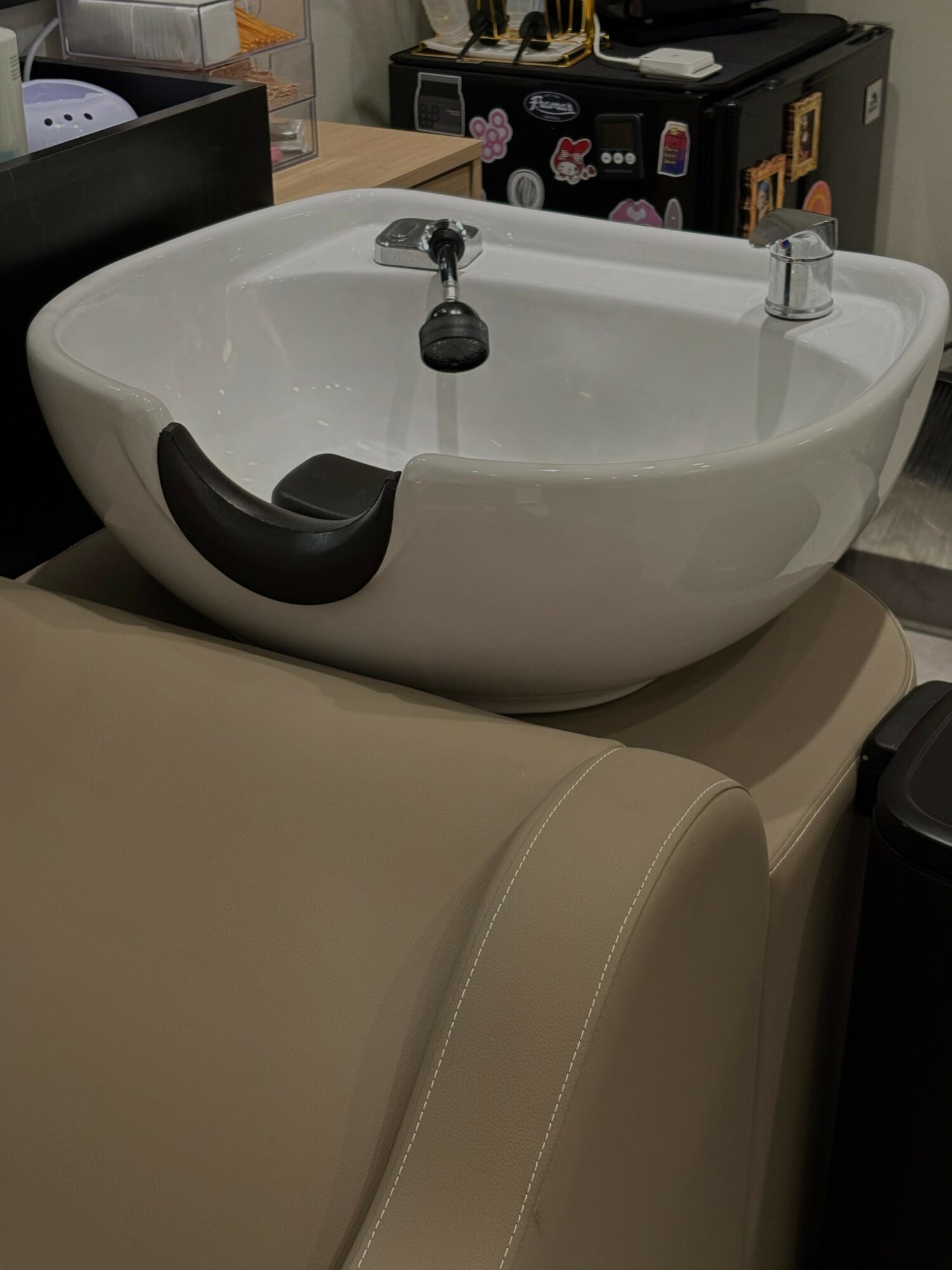 White sink with two faucets, black and gray objects inside, placed on a beige surface, in a room with various items.