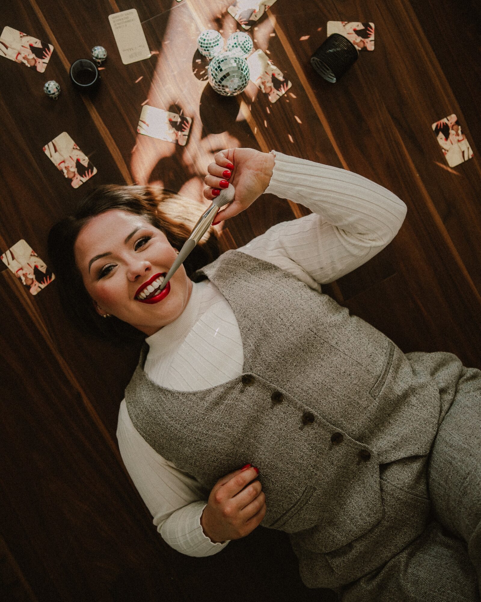 Woman lying on a wooden table, smiling, holding a knife, surrounded by photos, drinks, and decorations.