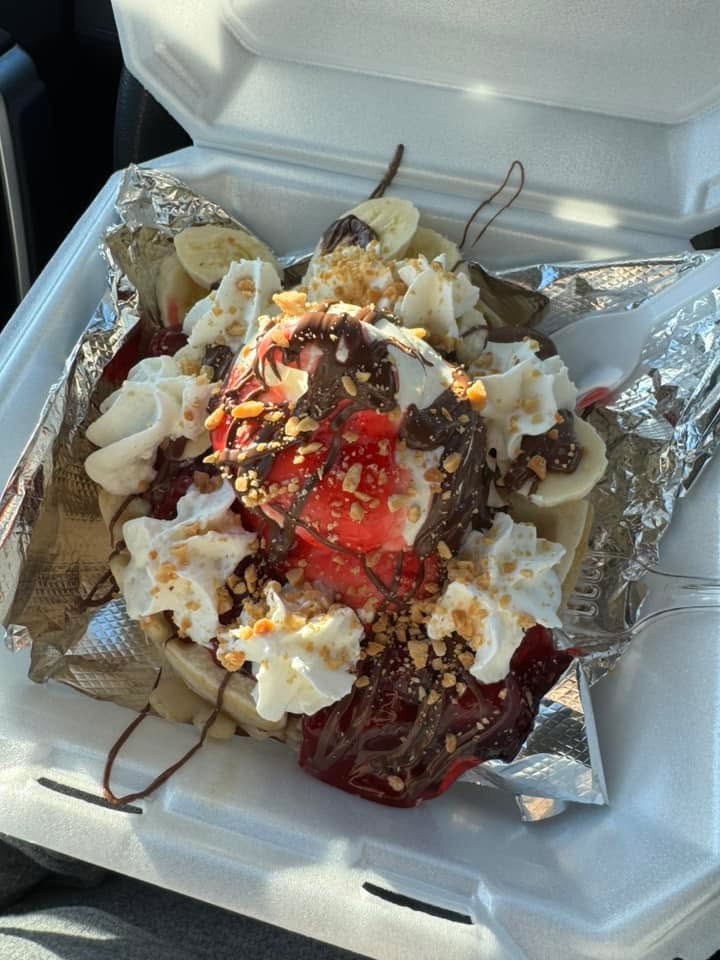 Dessert with ice cream, chocolate, strawberries, and toppings in a takeout container.