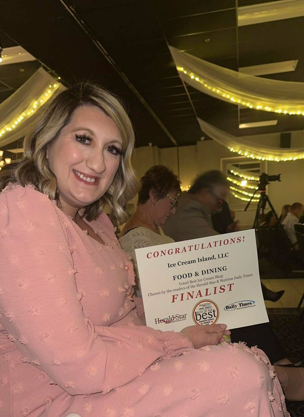 Woman in pink dress holding a certificate at an indoor event with decorative lighting.