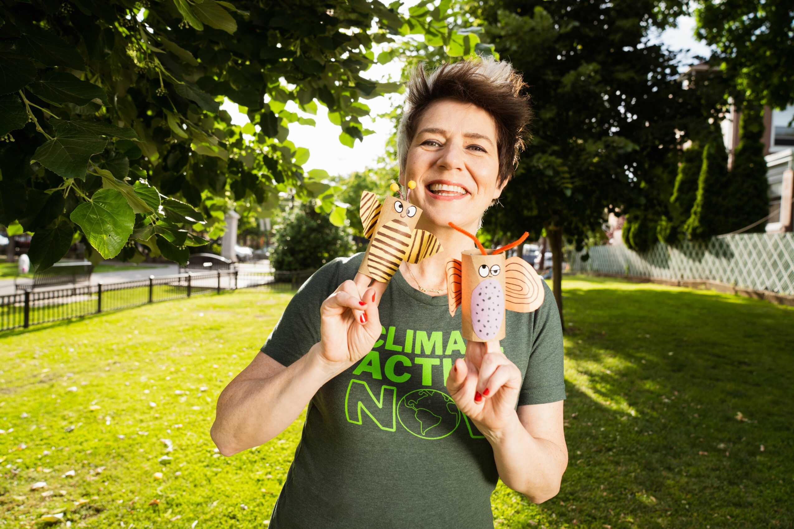 Smiling woman holding two ice cream cones outdoors in a park with trees and grass