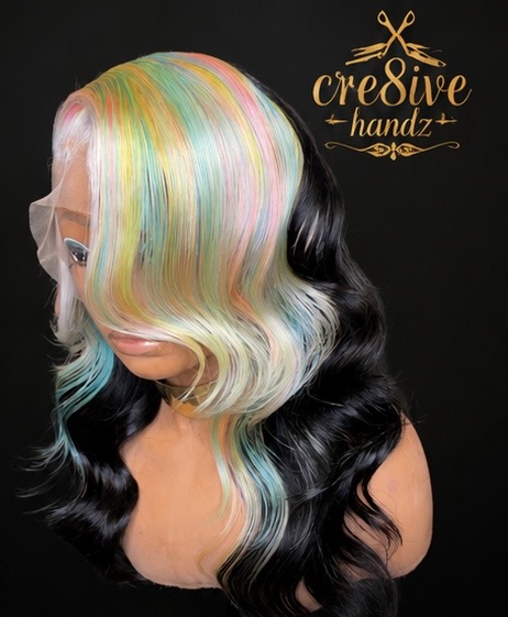 Woman with multicolored pastel hair on one side and black hair on the other, with a black background and gold logo.