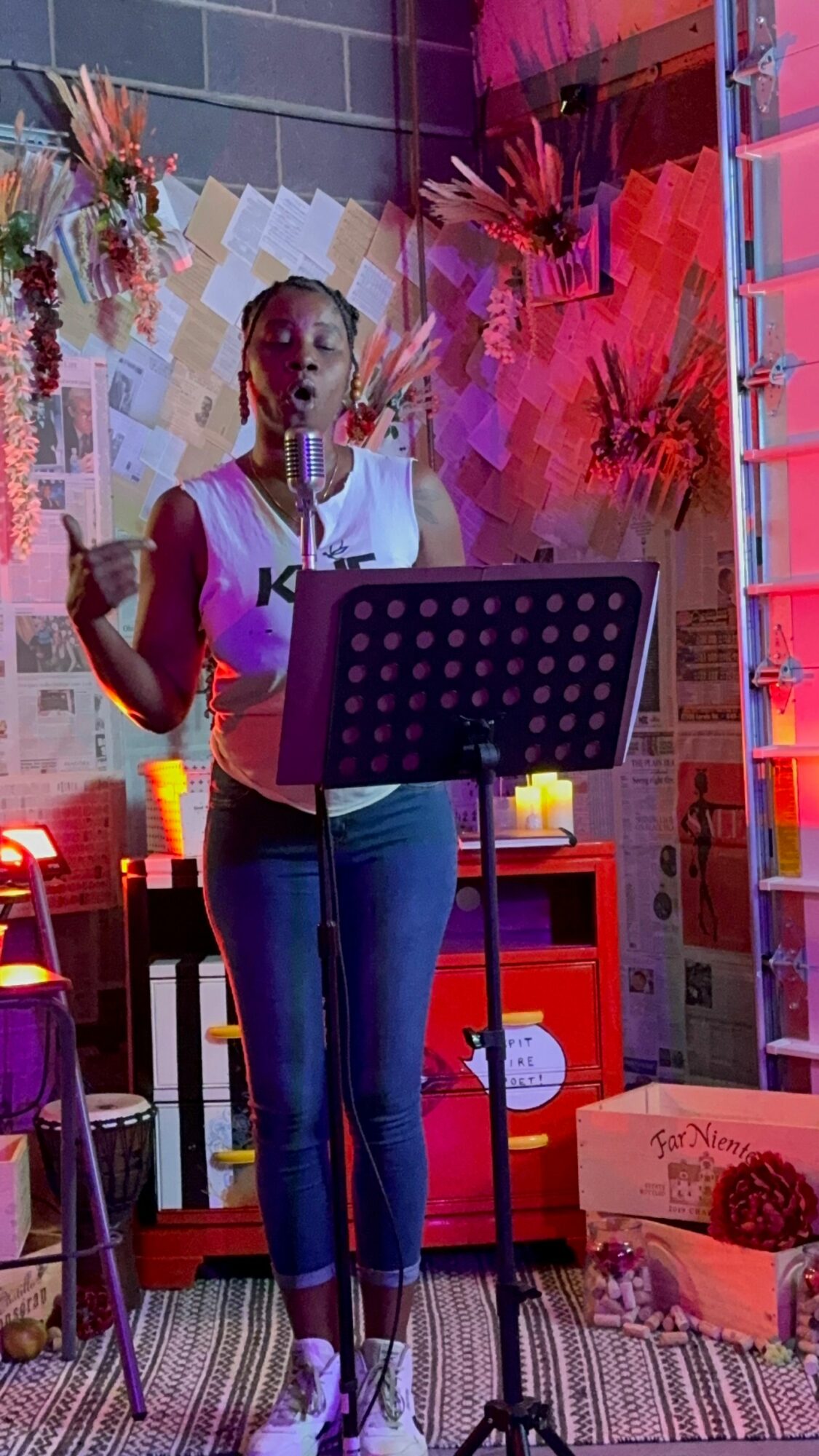 Woman standing in a room with pink and red decorations, holding a microphone, with a music stand in front of her.