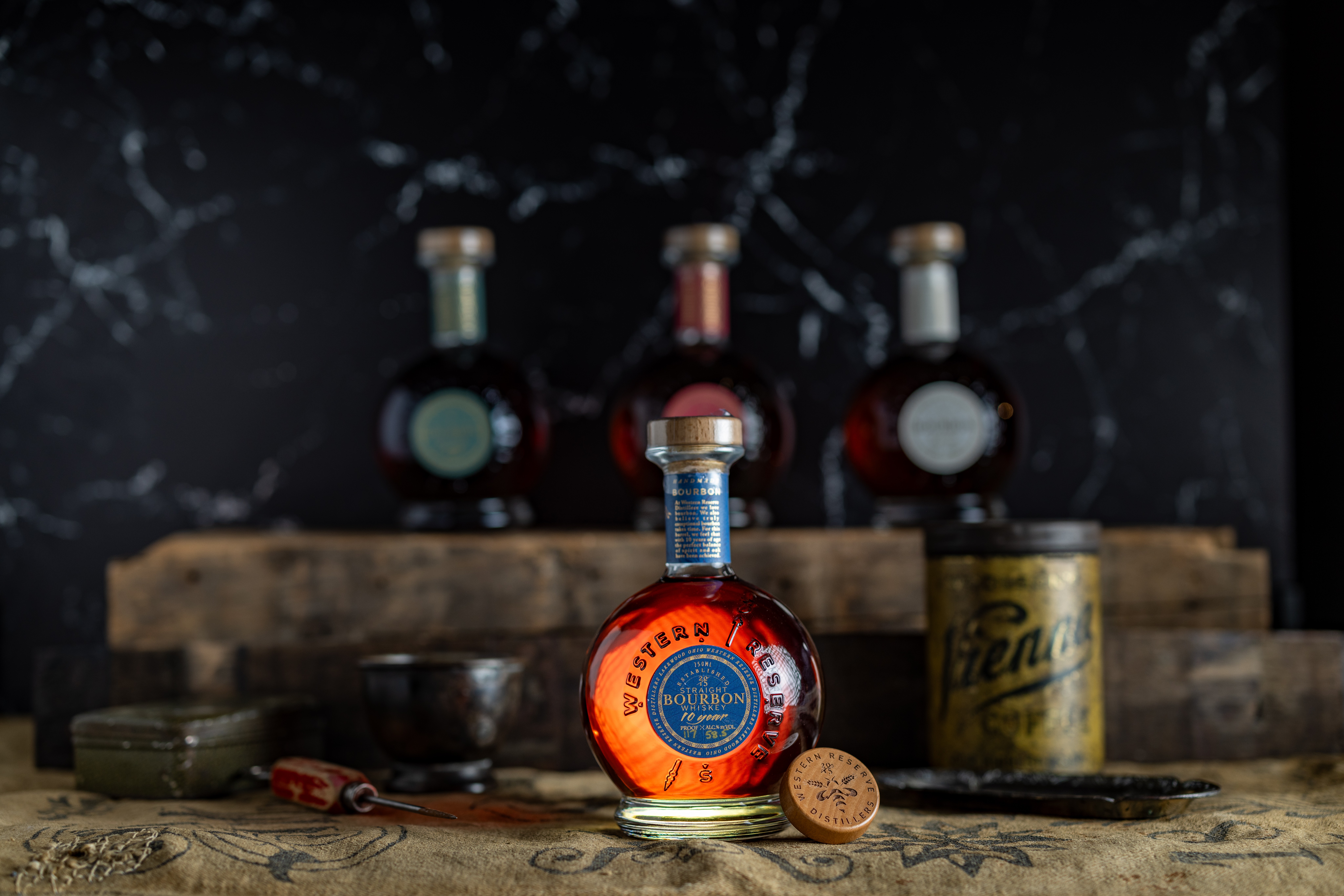 Three bottles of alcohol on a wooden surface with a dark marble background, one bottle in front with a coin nearby.