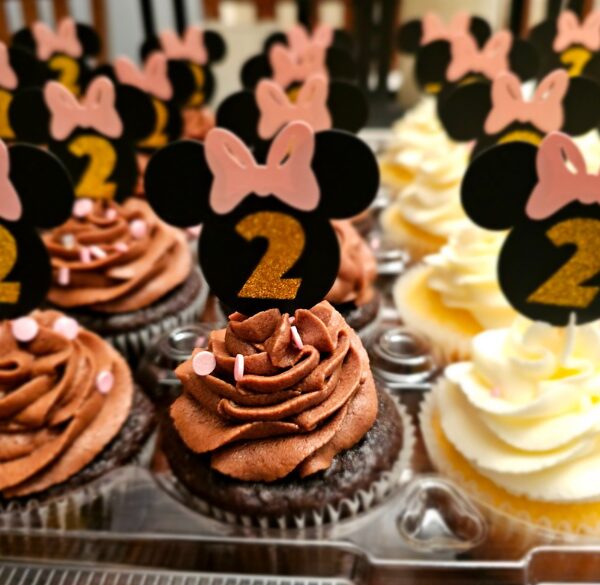 Chocolate and vanilla cupcakes with Minnie Mouse themed toppers, decorated with pink bows and number 2, on a display tray.