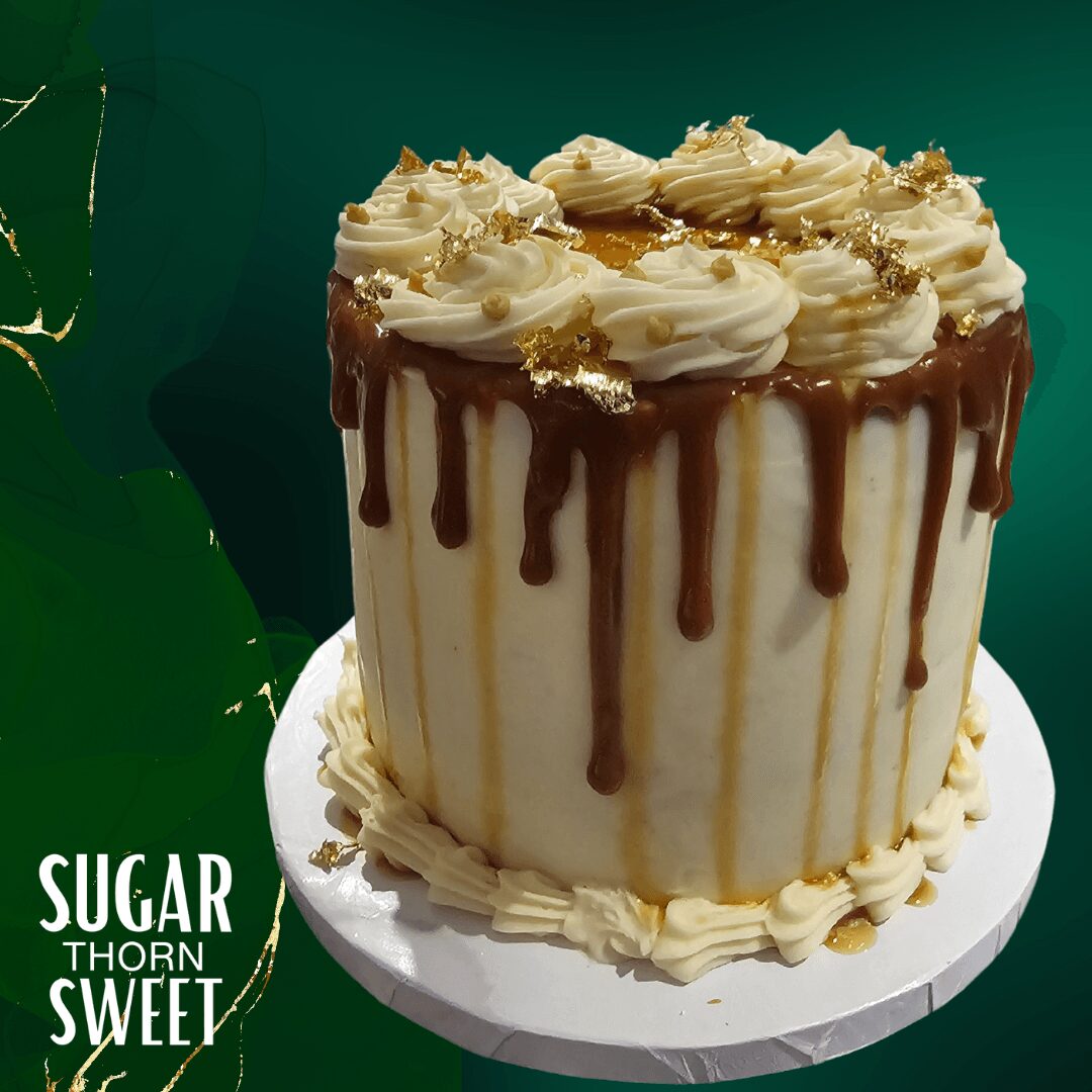 A tall cake with white frosting, chocolate drips, and cream decorations on top, on a white plate against a green background.