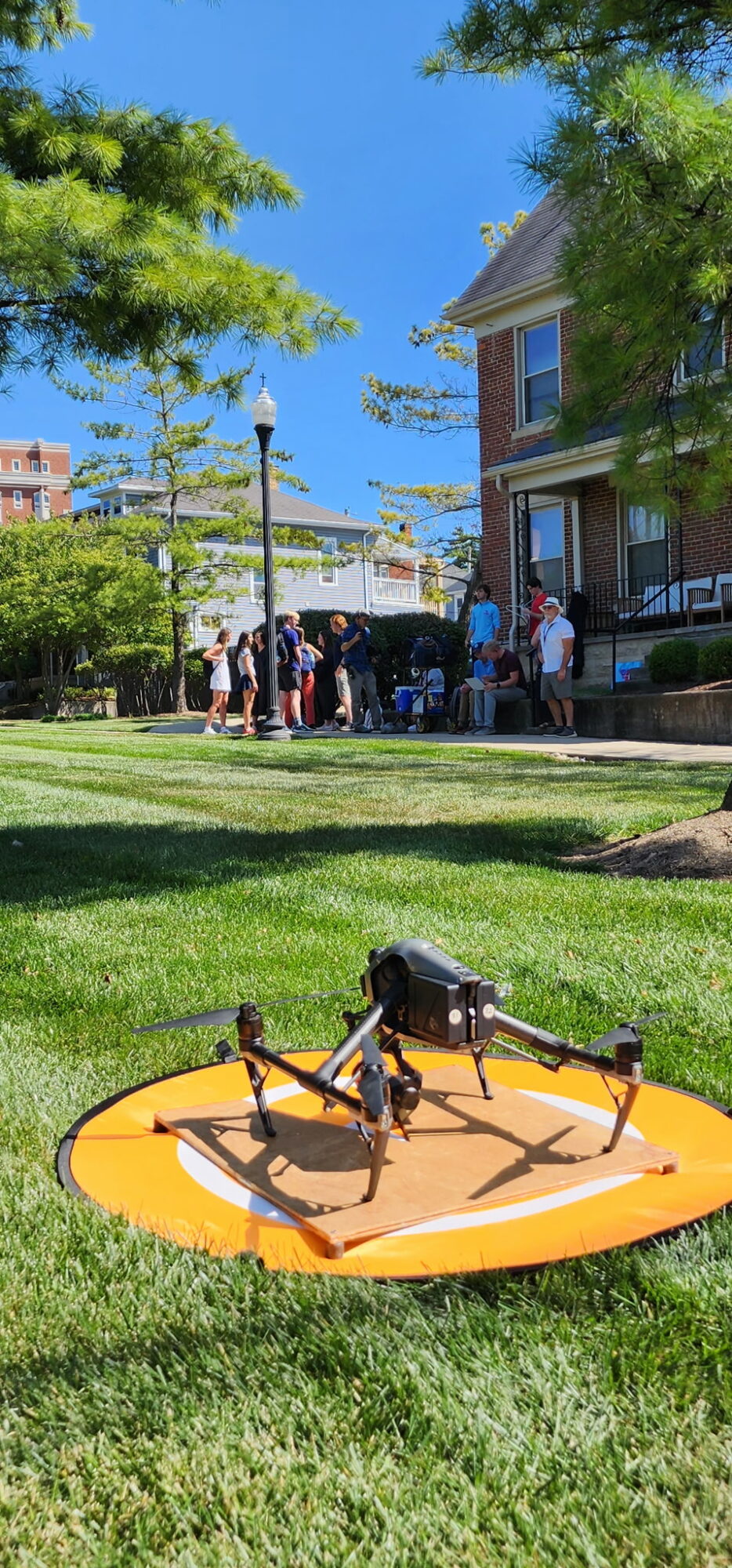Drones on a yellow mat in a park with people and buildings in the background.