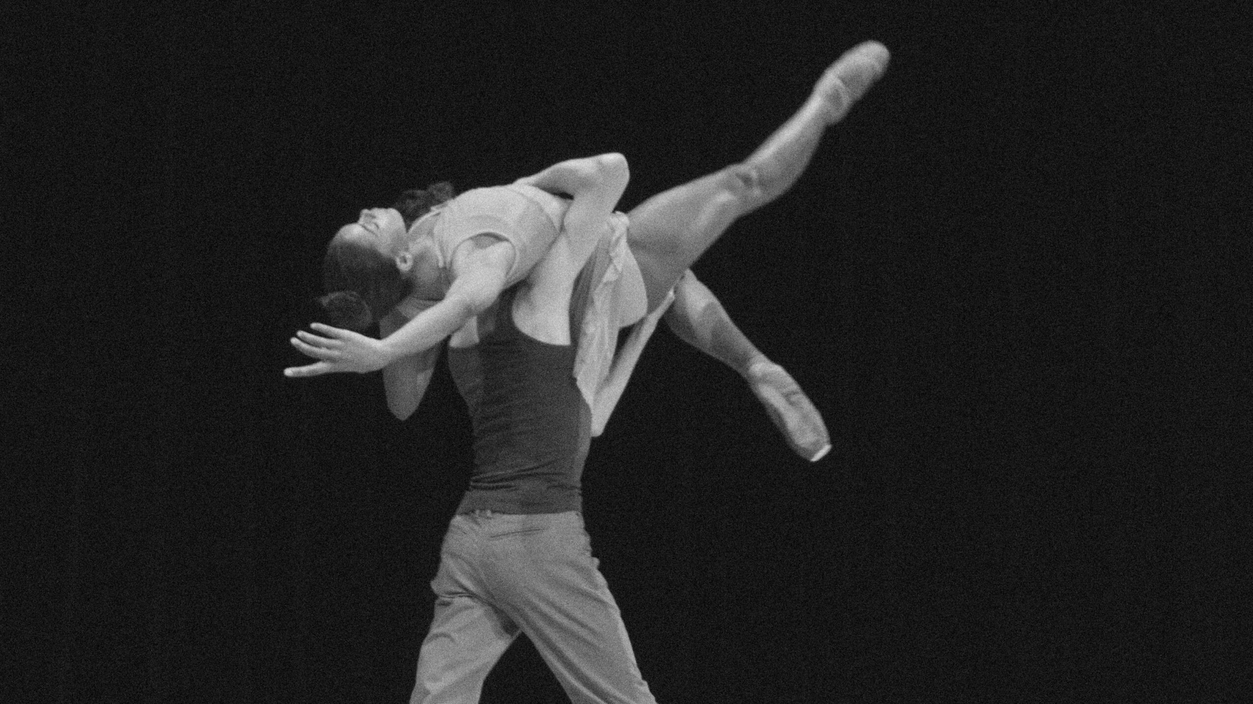 Two ballet dancers perform an acrobatic lift on stage, with one dancer elevated horizontally and the other supporting.