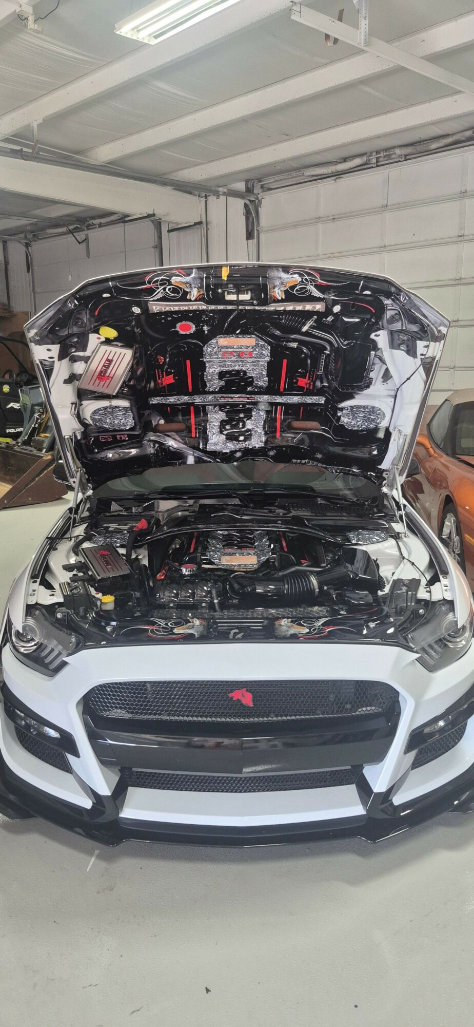 Front view of a car with its hood open, showing engine components, in a garage or workshop.