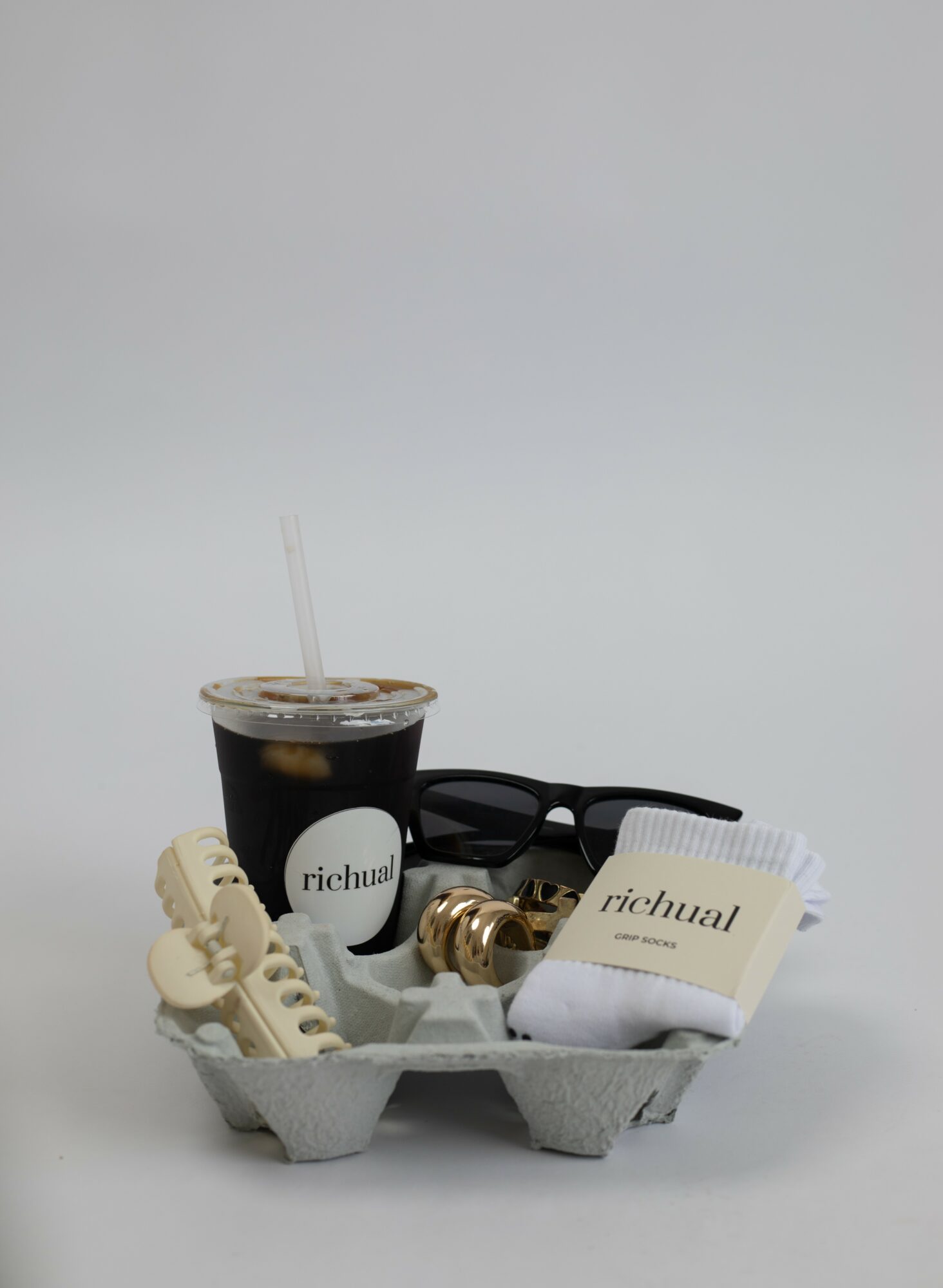 Tray with sunglasses, a cup of iced coffee, a watch, and a small box, against a plain background.