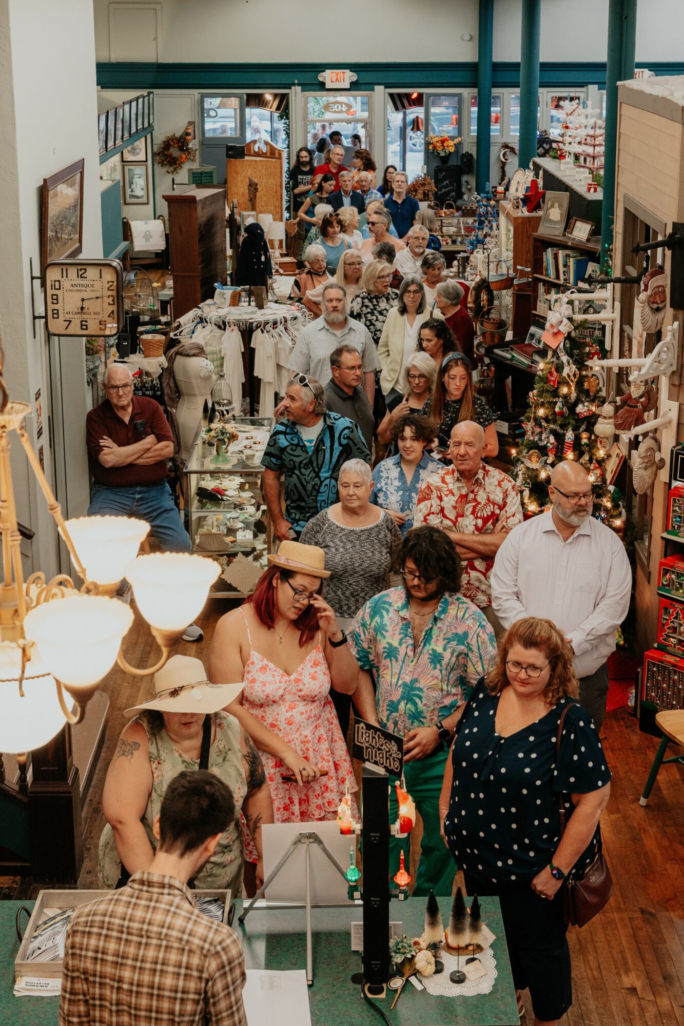 Crowd of people shopping inside a store with shelves and displays, some browsing and others walking, in a busy retail environment.