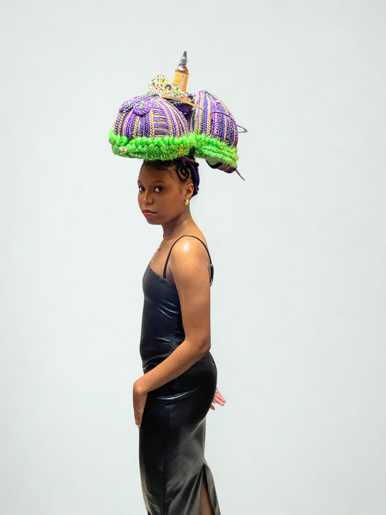 Young girl wearing a large, colorful, beaded hat resembling a decorated pumpkin, standing against a plain background.