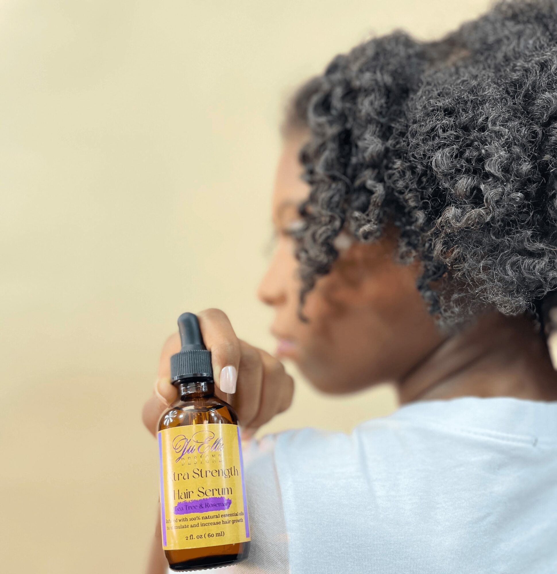 Person with curly hair holding a small amber bottle with a dropper, facing sideways, blurred background.