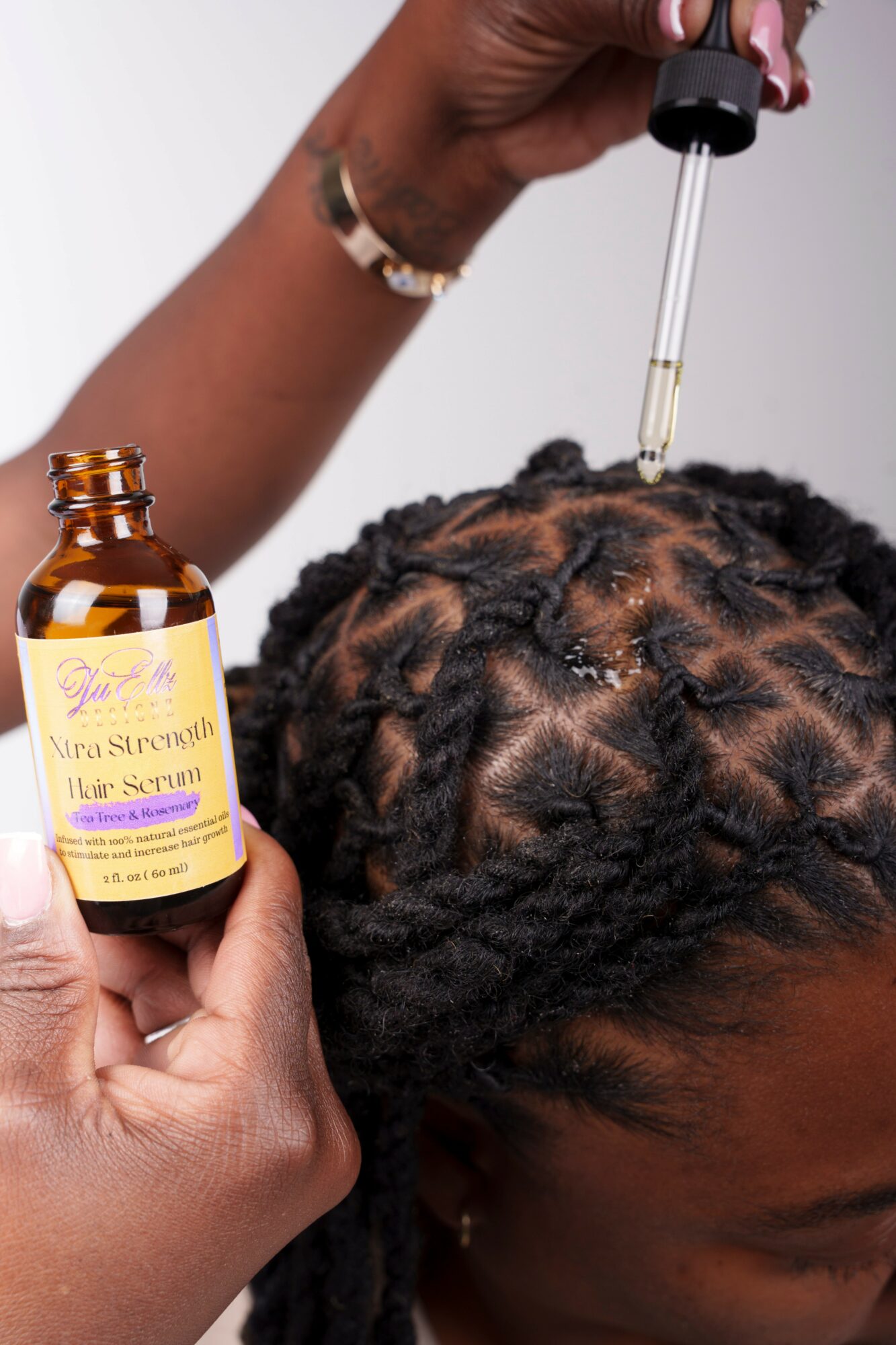 Person applying hair oil with a dropper to braided hair, holding a bottle labeled 'Nira Strength Hair Oil'.