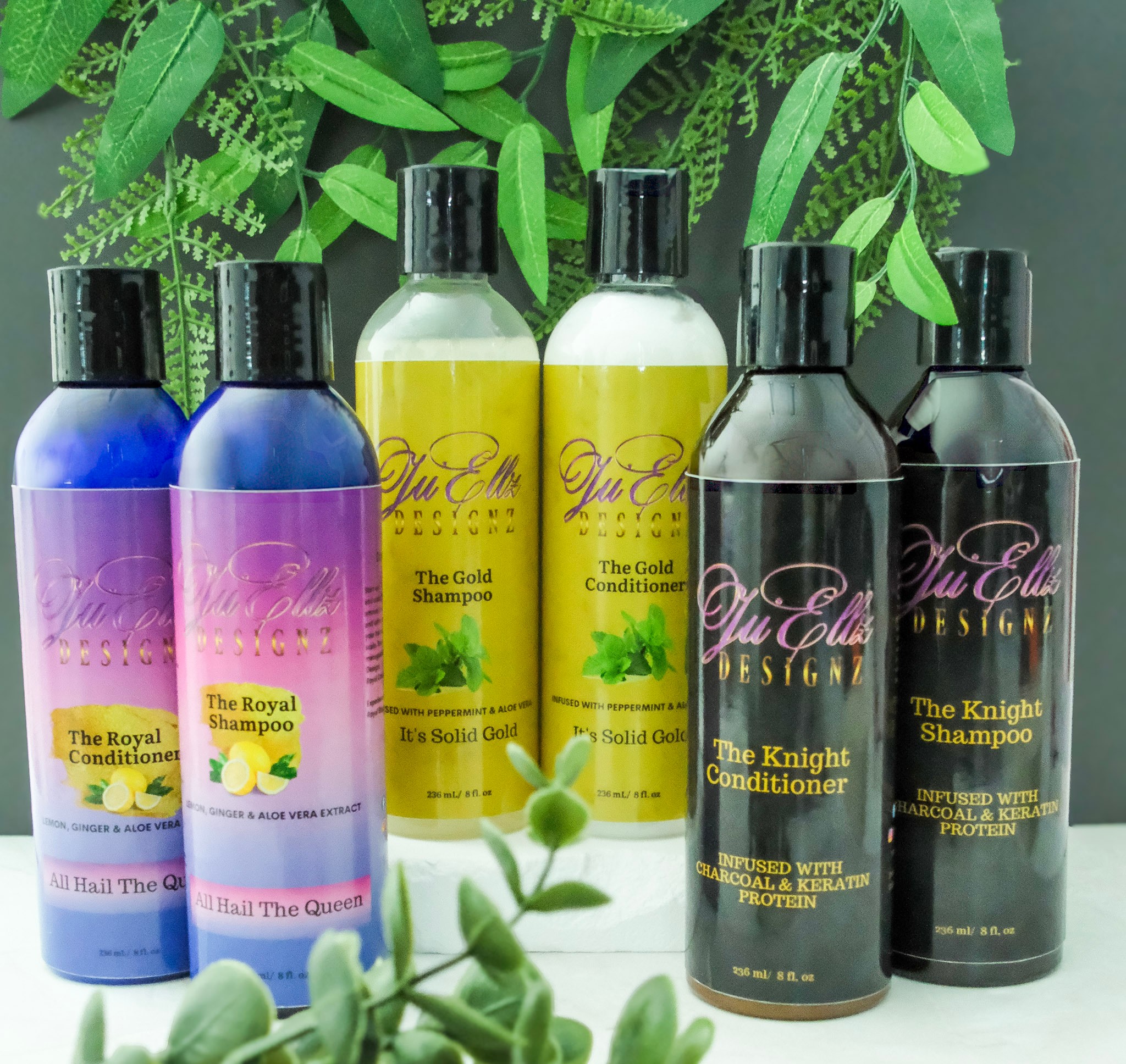 Six bottles of hair care products with colorful labels, set against green foliage background.