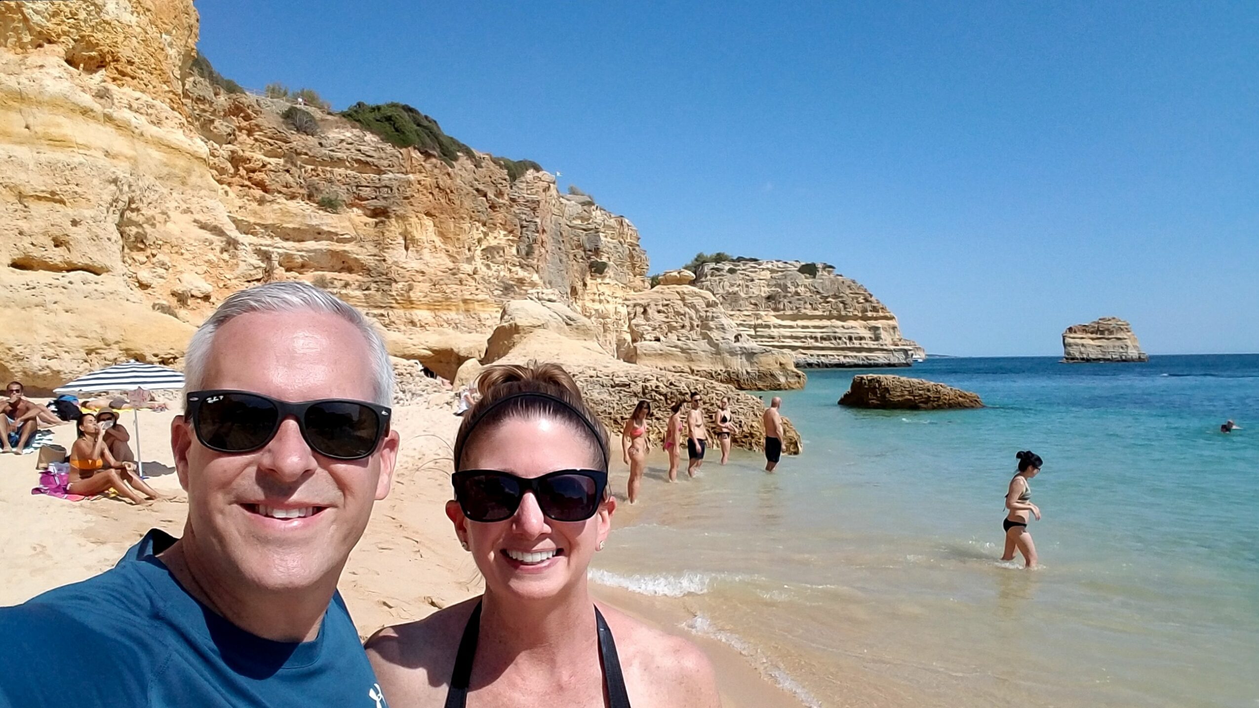 Two people smiling at the beach with cliffs and ocean in the background.
