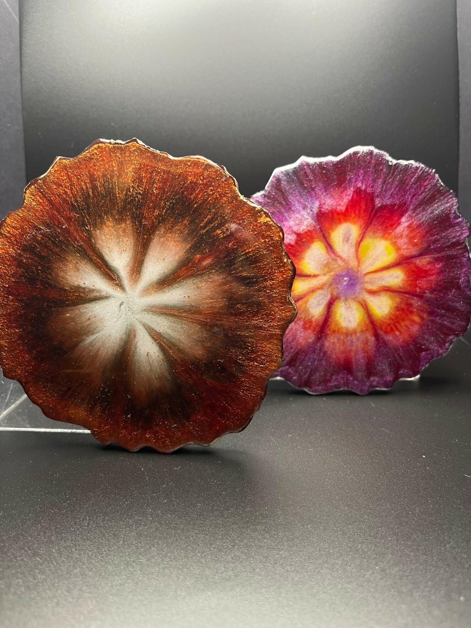 Two colorful mushroom caps with vibrant patterns and textures, placed on a black surface against a dark background.