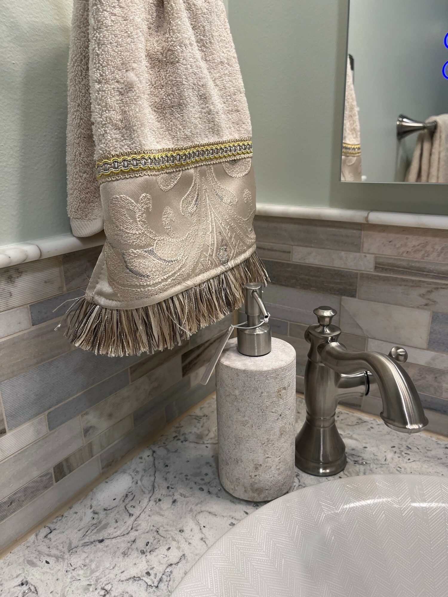 Towel hanging on a bathroom wall above a marble countertop with a soap dispenser and faucet.