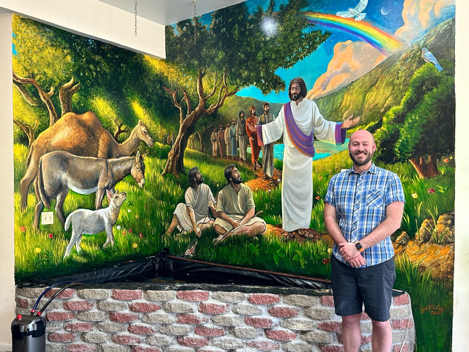 Two men sit on grass with a man in white robes standing with open arms, surrounded by animals and a colorful landscape.