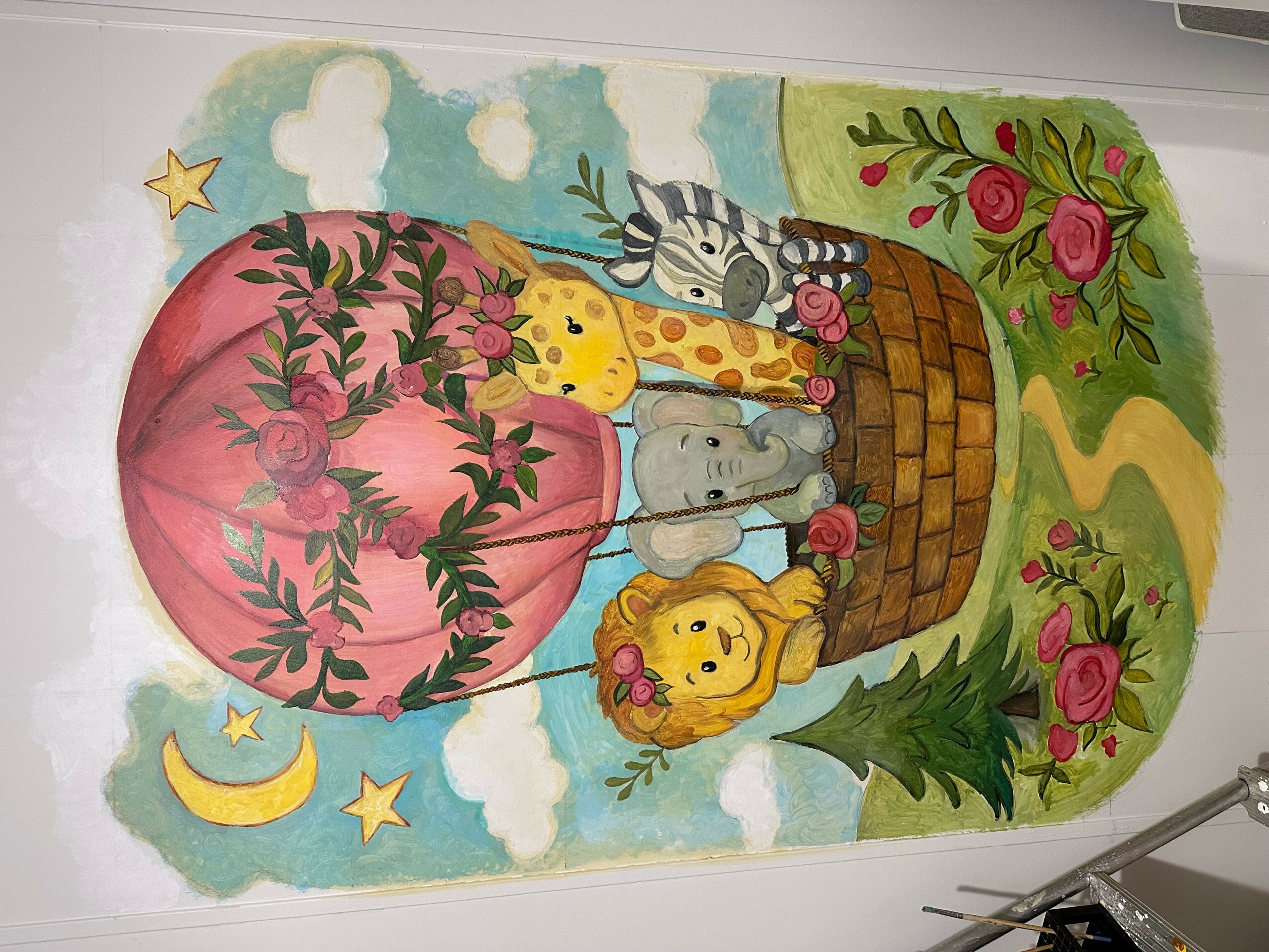 Colorful mural with animals, a hot air balloon, flowers, and a rainbow, featuring a lion, zebra, giraffe, and elephant.