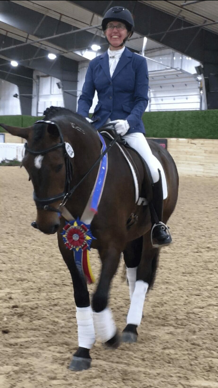 Person in formal riding attire on a decorated horse in an indoor arena.
