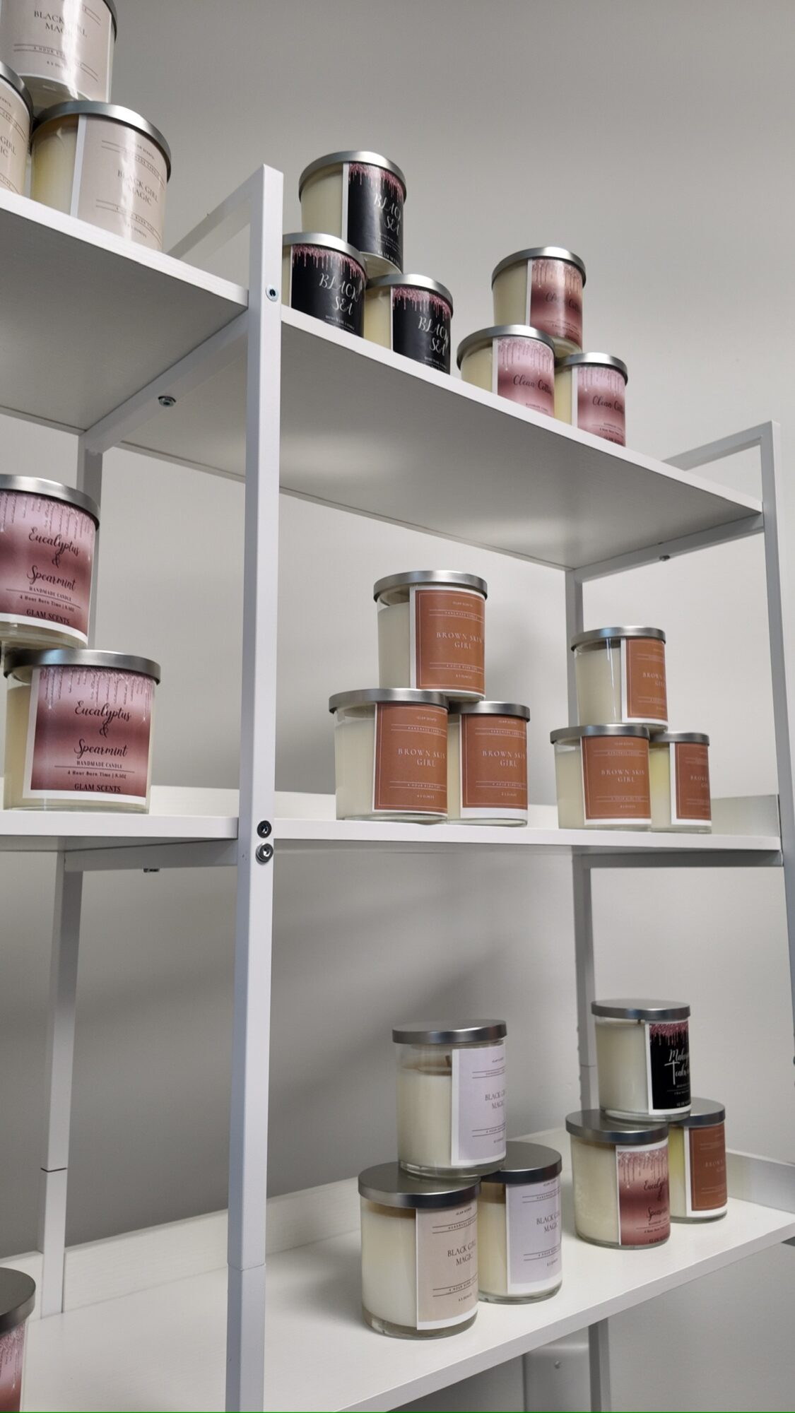 Shelves with jars containing various powders or spices, arranged in rows and stacks, against a plain wall.