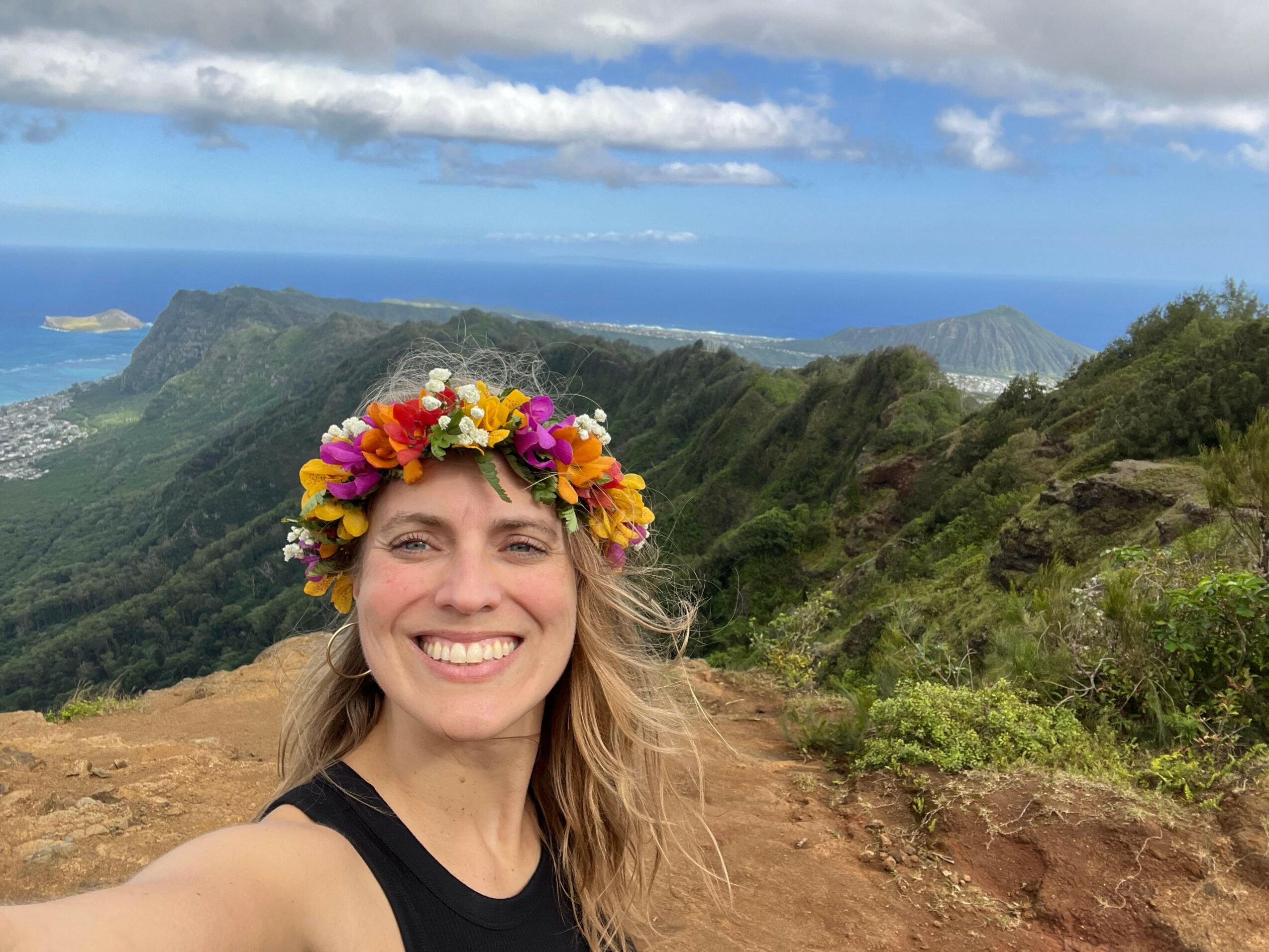 Smiling woman with a colorful flower crown outdoors, landscape with hills and sky in background, upside down.