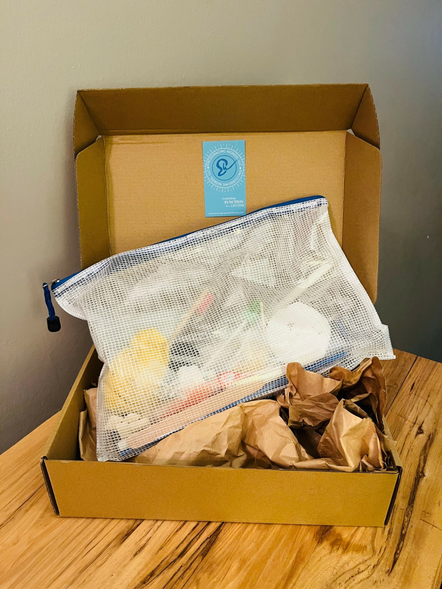 Open cardboard box with a mesh bag containing various items inside, on a wooden surface.