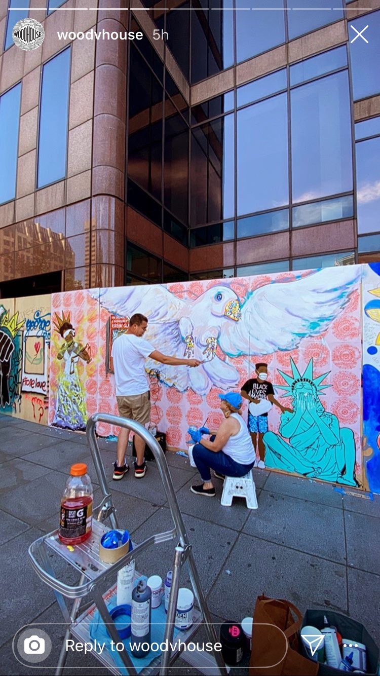 Two people painting a colorful mural on a wall with a large bird and Statue of Liberty, in an urban setting.