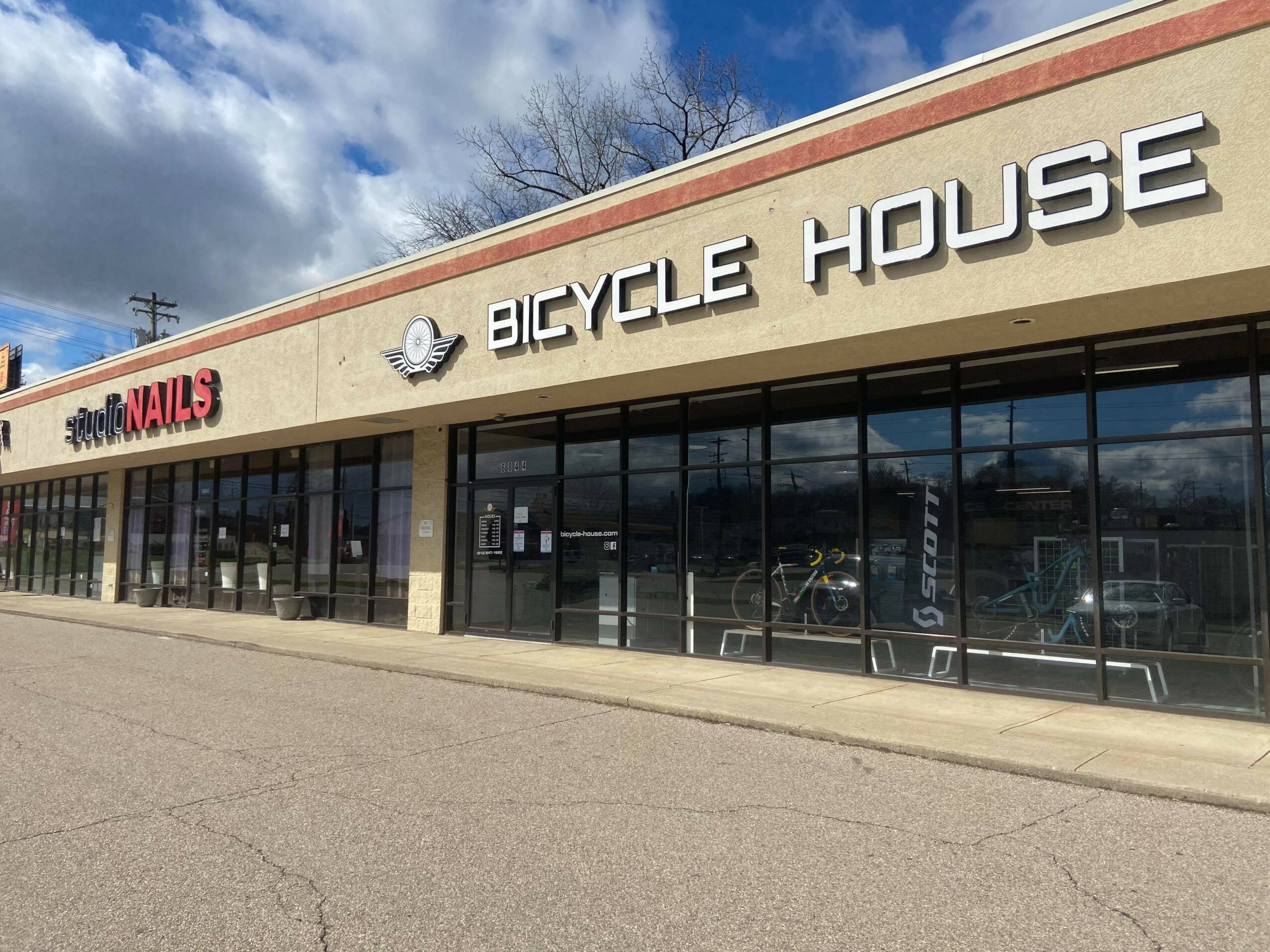 Storefront with large glass windows and signs for 'Bicycle House' and 'Nails' on a brick building.