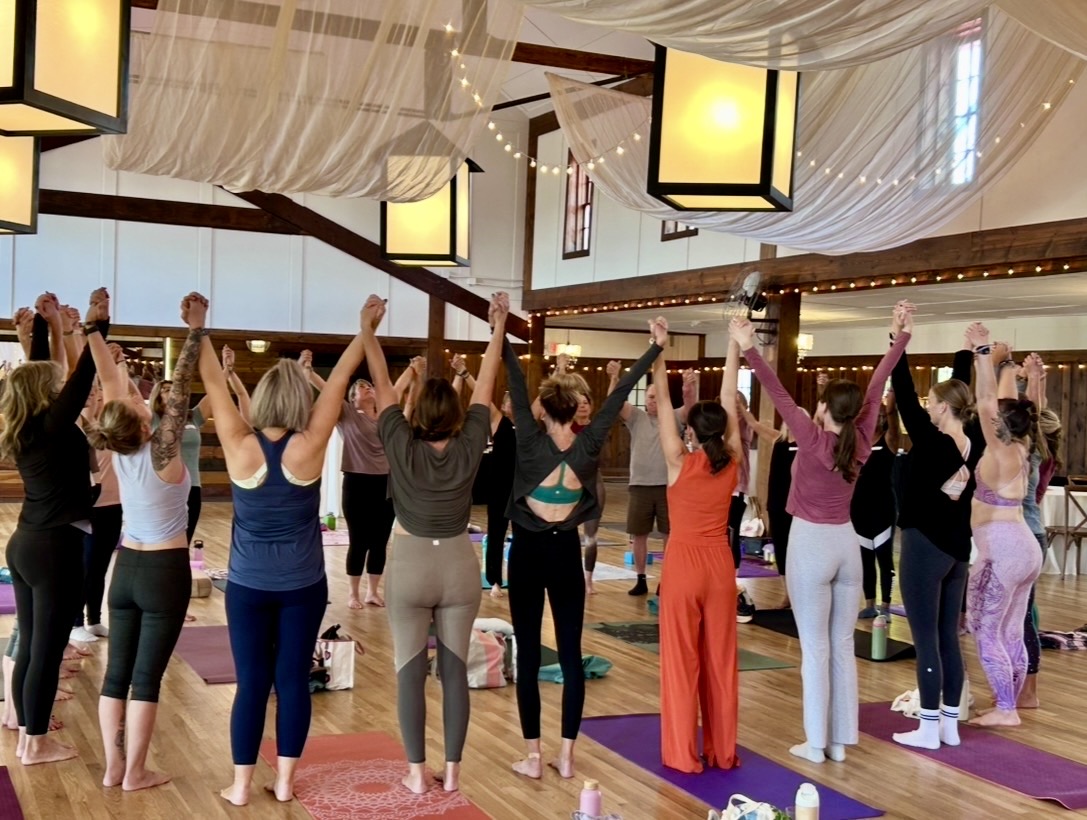 Group of people practicing yoga in a spacious, well-lit studio with hanging lanterns and draped ceiling fabric.