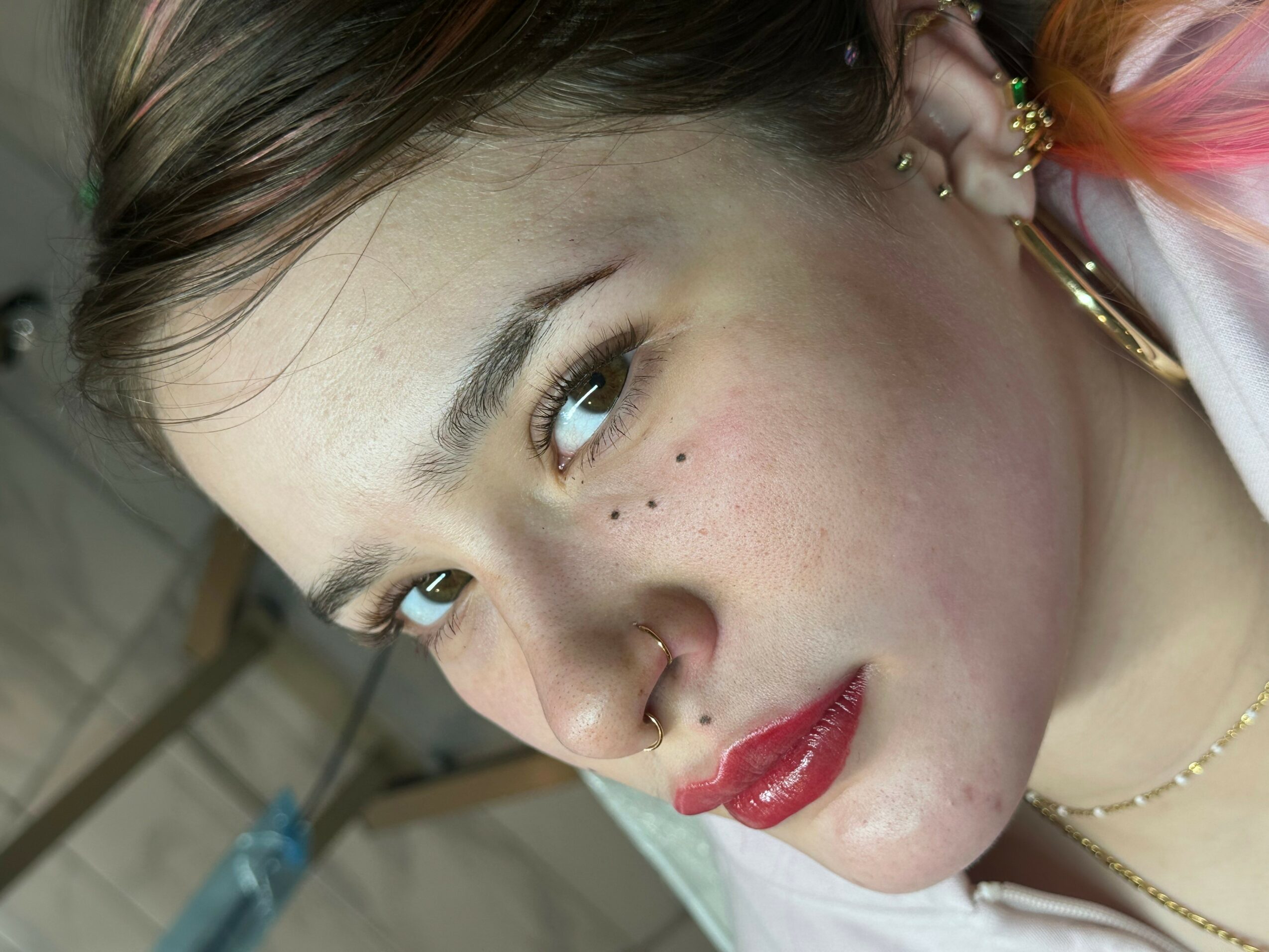 Close-up of a young woman with makeup, earrings, and freckles, looking sideways with a slight smile.