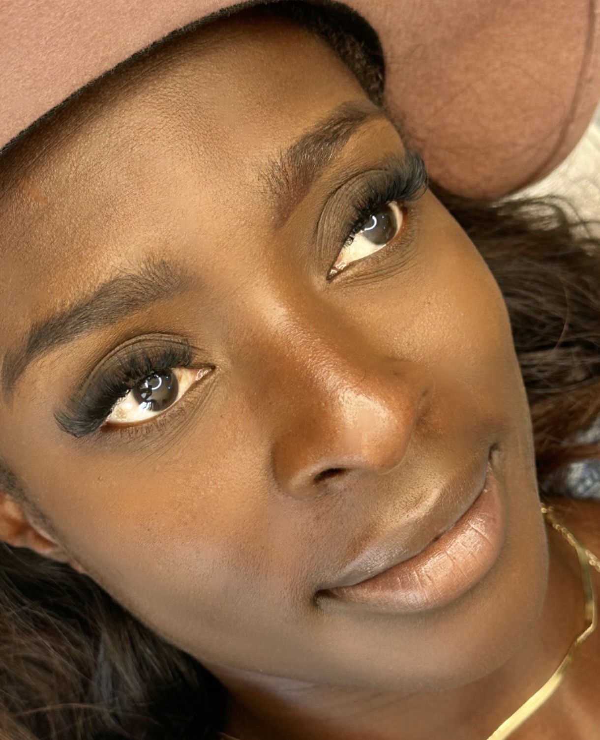 Close-up of a woman with makeup, lying down, wearing a hat, looking upward, with a neutral expression.