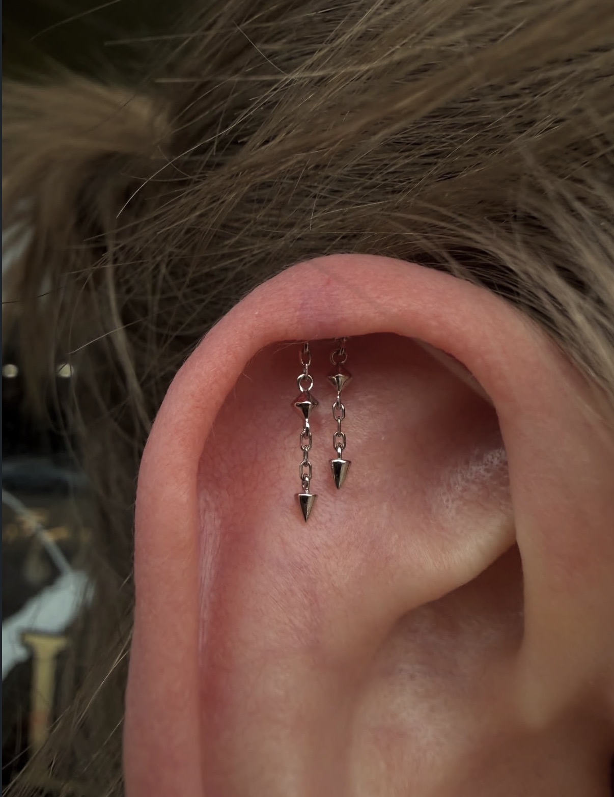 Close-up of a person's ear with dangling spike earrings, hair partially covering the ear.