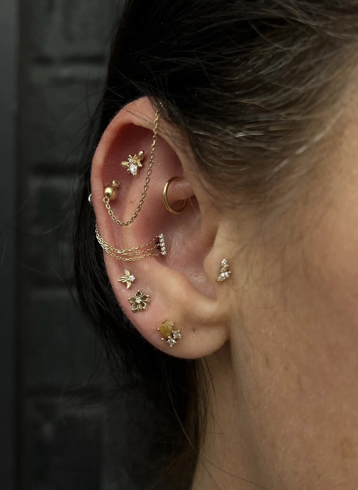Close-up of a person's ear with multiple earrings and jewelry, including a chain and decorative studs.