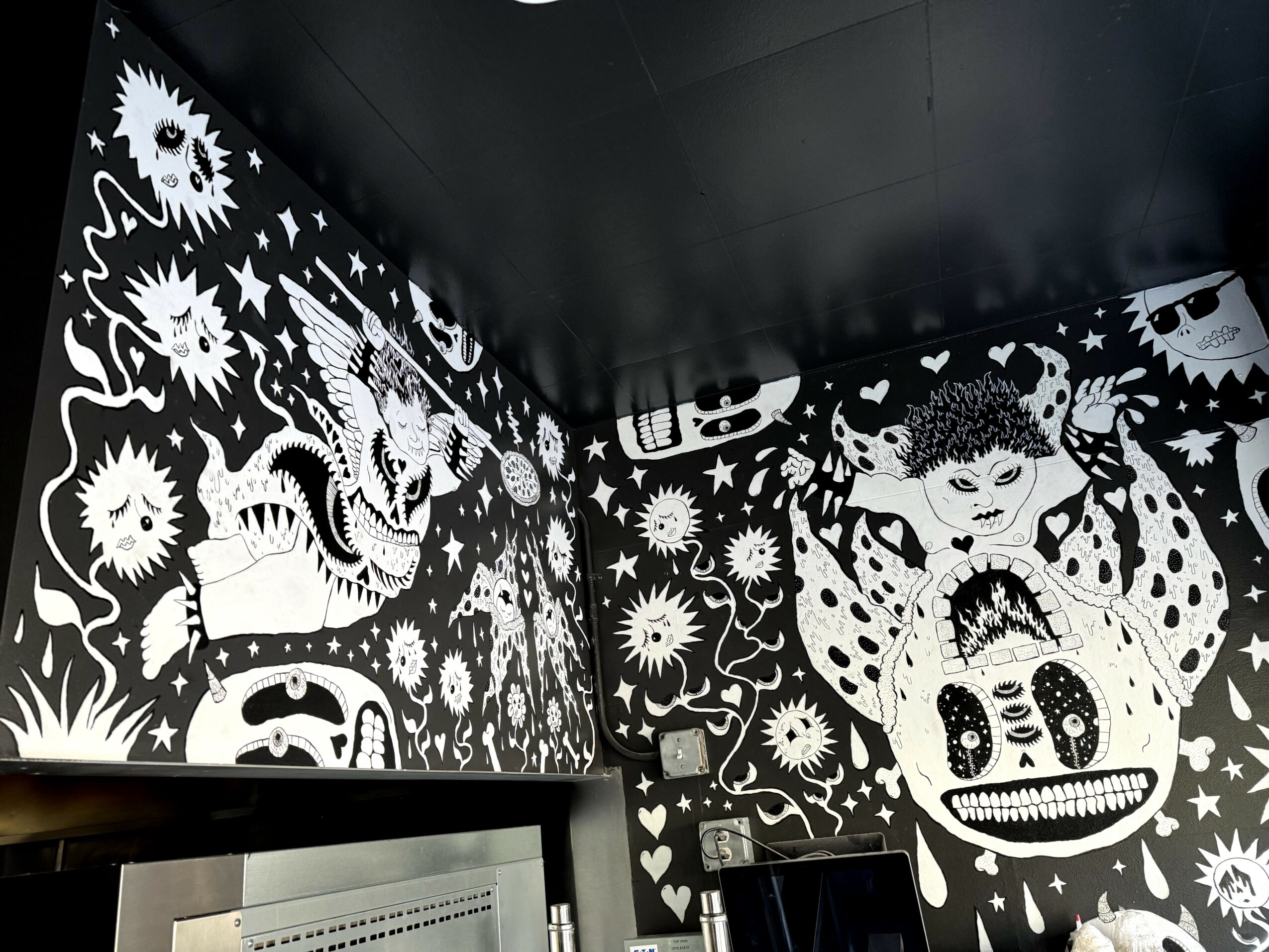 Black ceiling and walls with white illustrations of skulls, suns, and abstract designs, creating a mural-like effect.