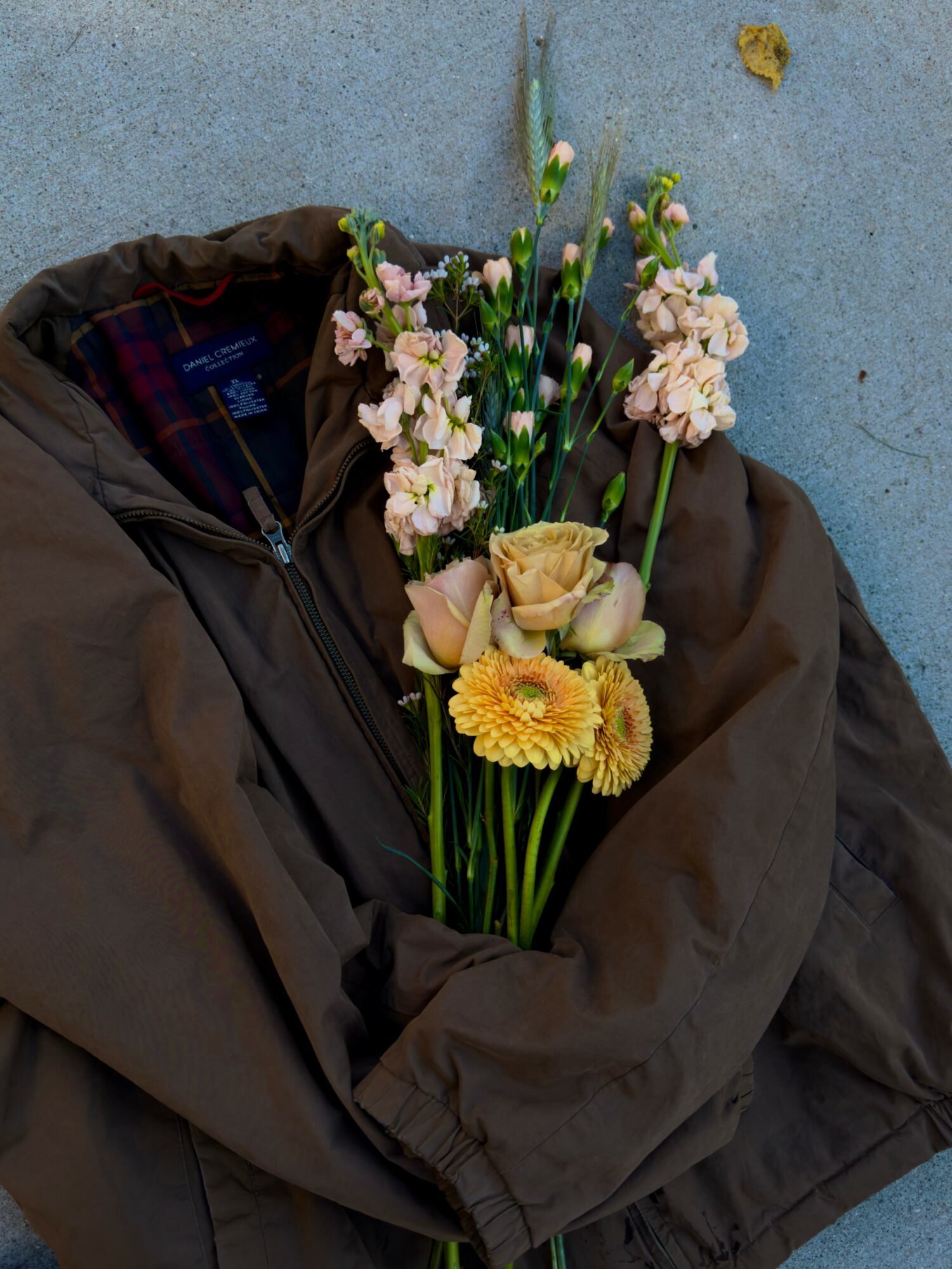 Person wearing a dark jacket holding a bouquet of pink, yellow, and white flowers against a blue background.