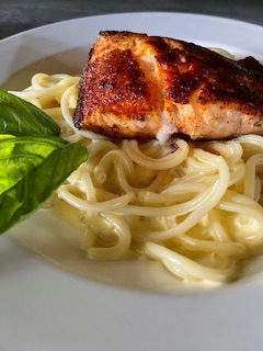 Grilled fish fillet on spaghetti with basil leaves on a white plate.