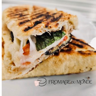 Grilled sandwich with melted cheese, vegetables, and bread grill marks, on a white plate with text logo.